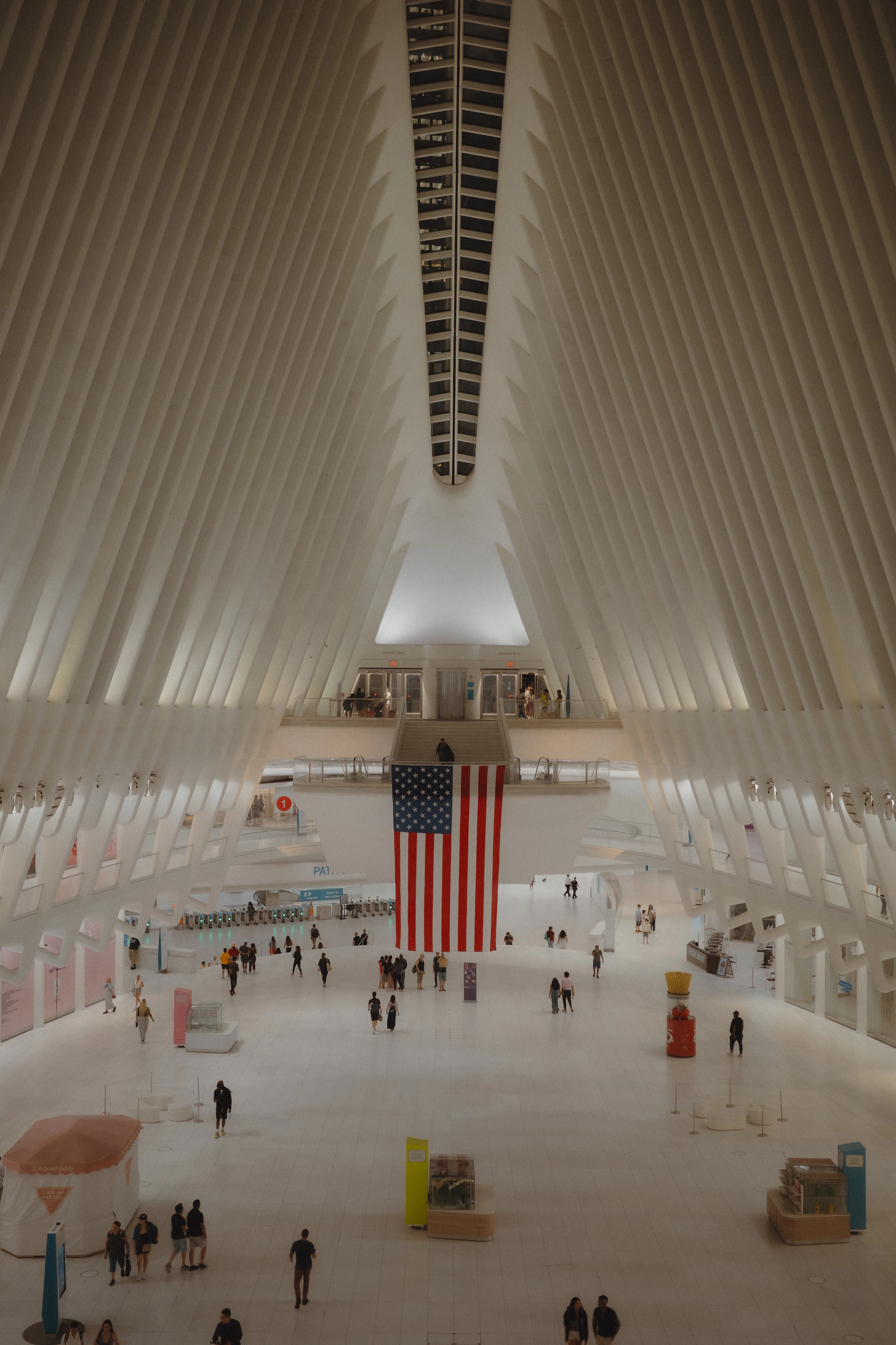 The white ribbed interior of the Oculus at the World Trade Center Transportation Hub in Lower Manhattan, its steel ribs converging on a skylight above a huge American flag hung over the concourse