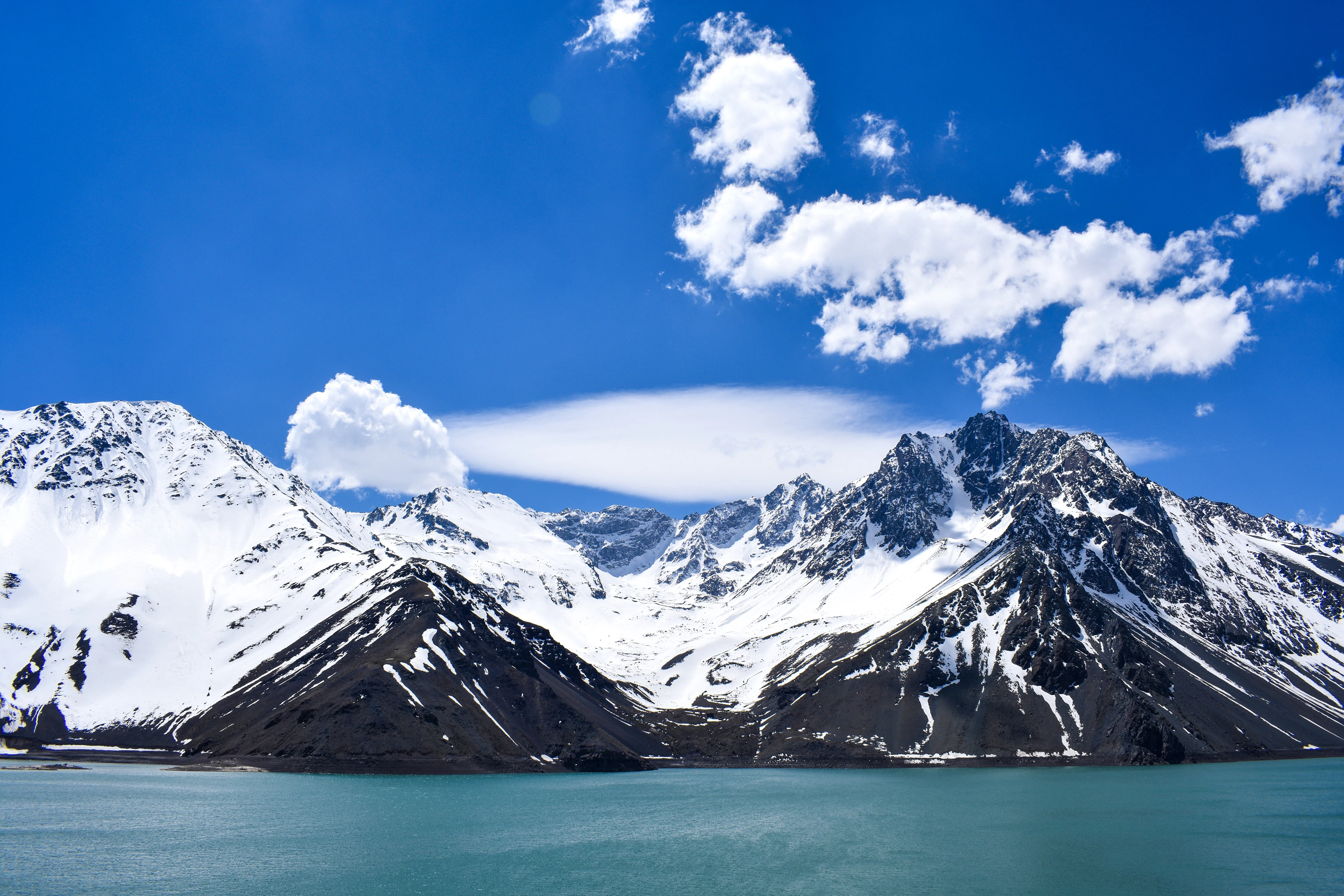 Snow-covered Andean peaks and a lens-shaped cloud above the pale turquoise water of a reservoir in the Cajon del Maipo, the mountain valley on Santiago's doorstep.