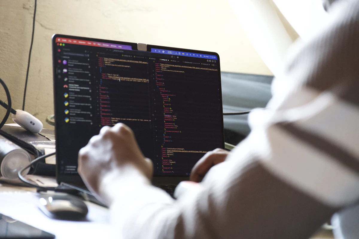 Tangan mengetik di keyboard laptop dengan kode program di layar