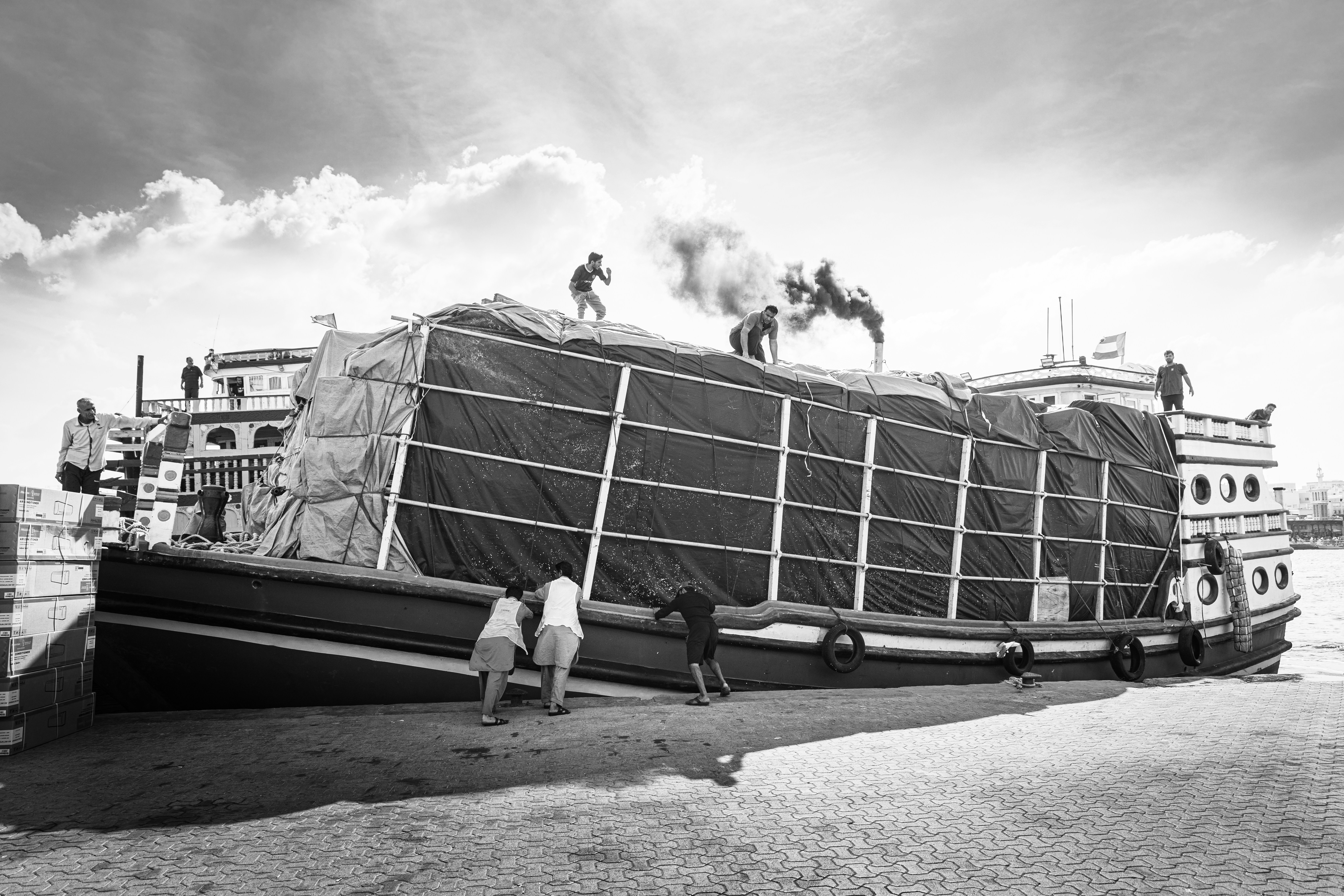 Workers loading a large cargo boat emitting smoke.