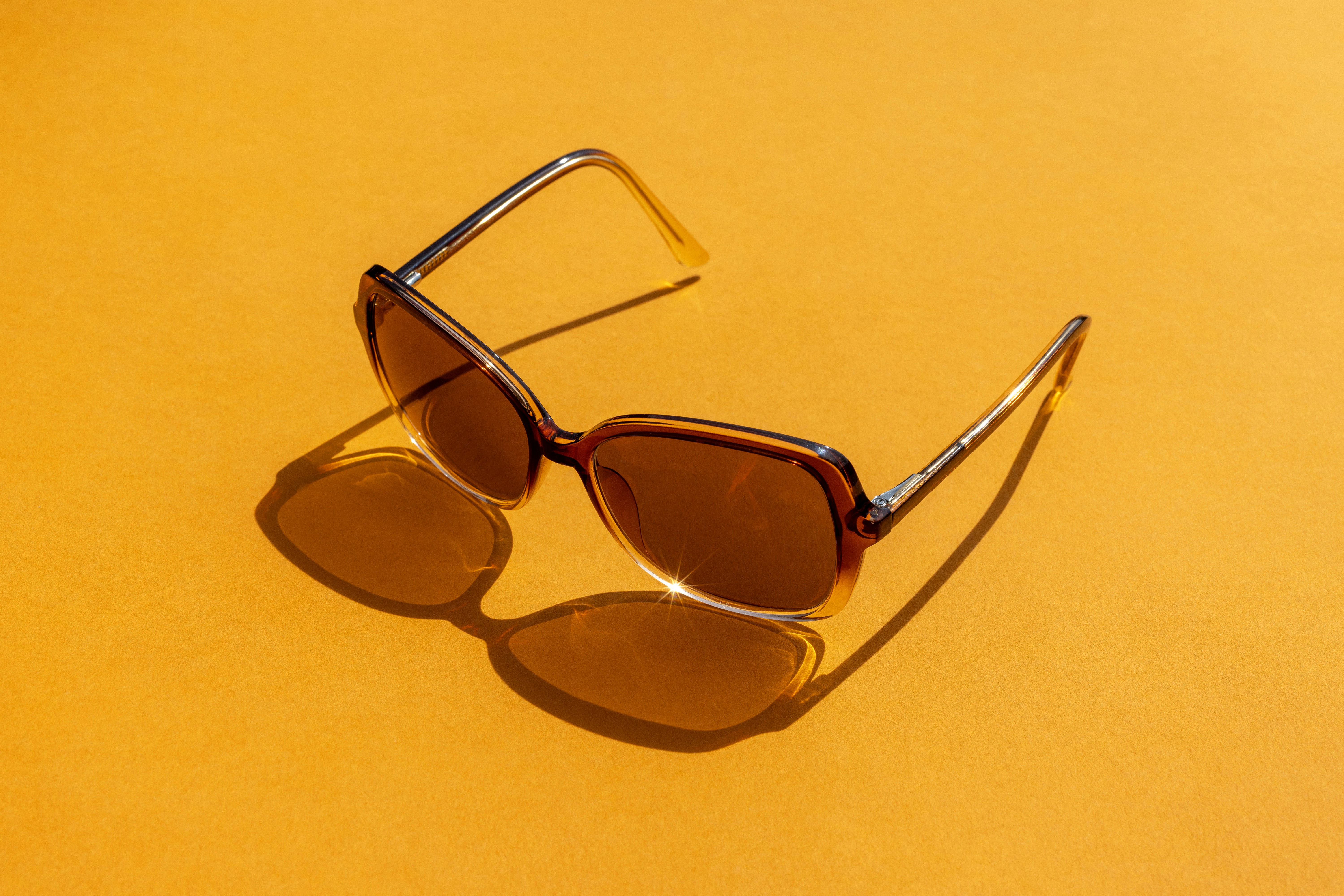 Brown sunglasses casting a shadow on a vibrant orange background.