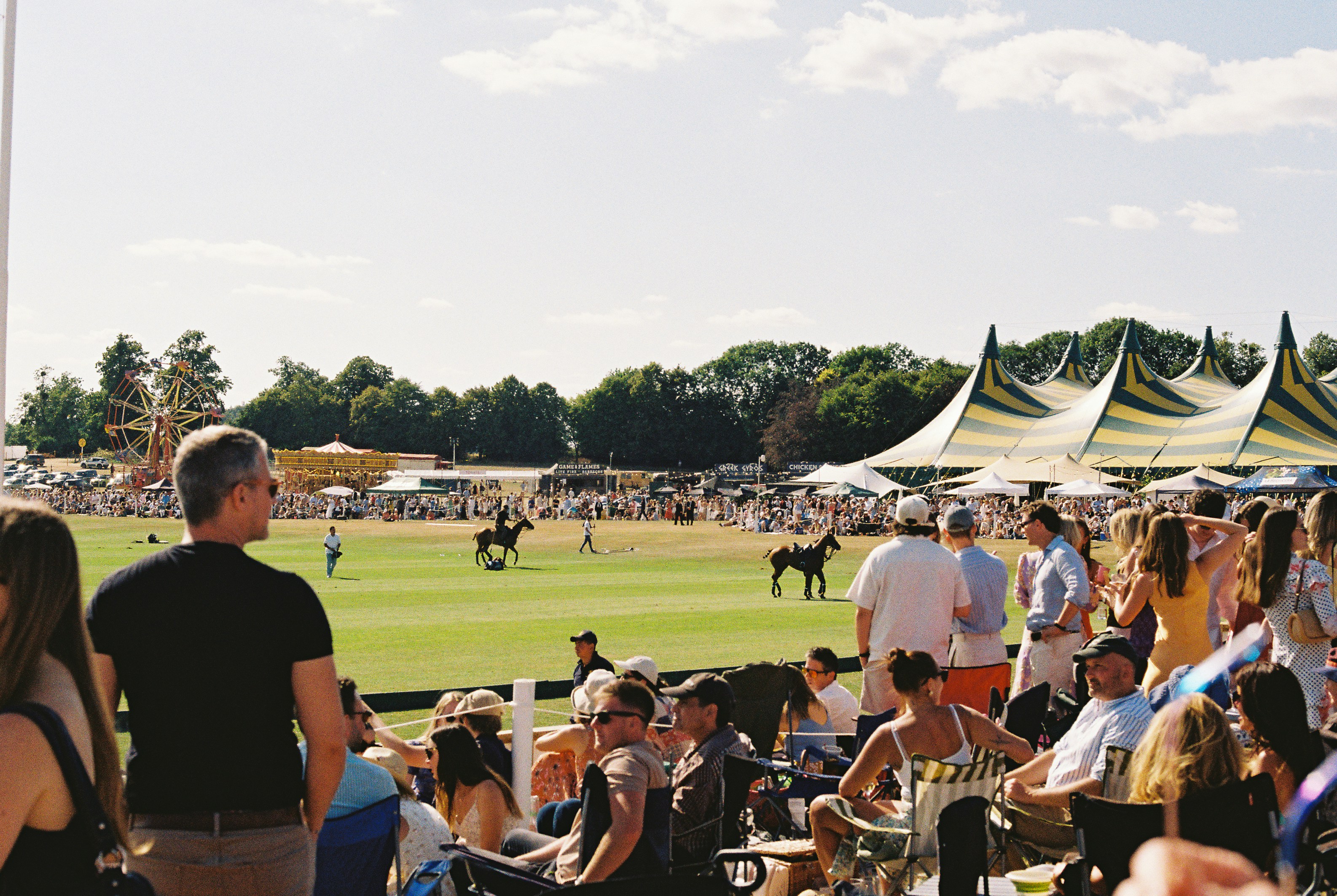 Spectators watching a polo match under striped tents