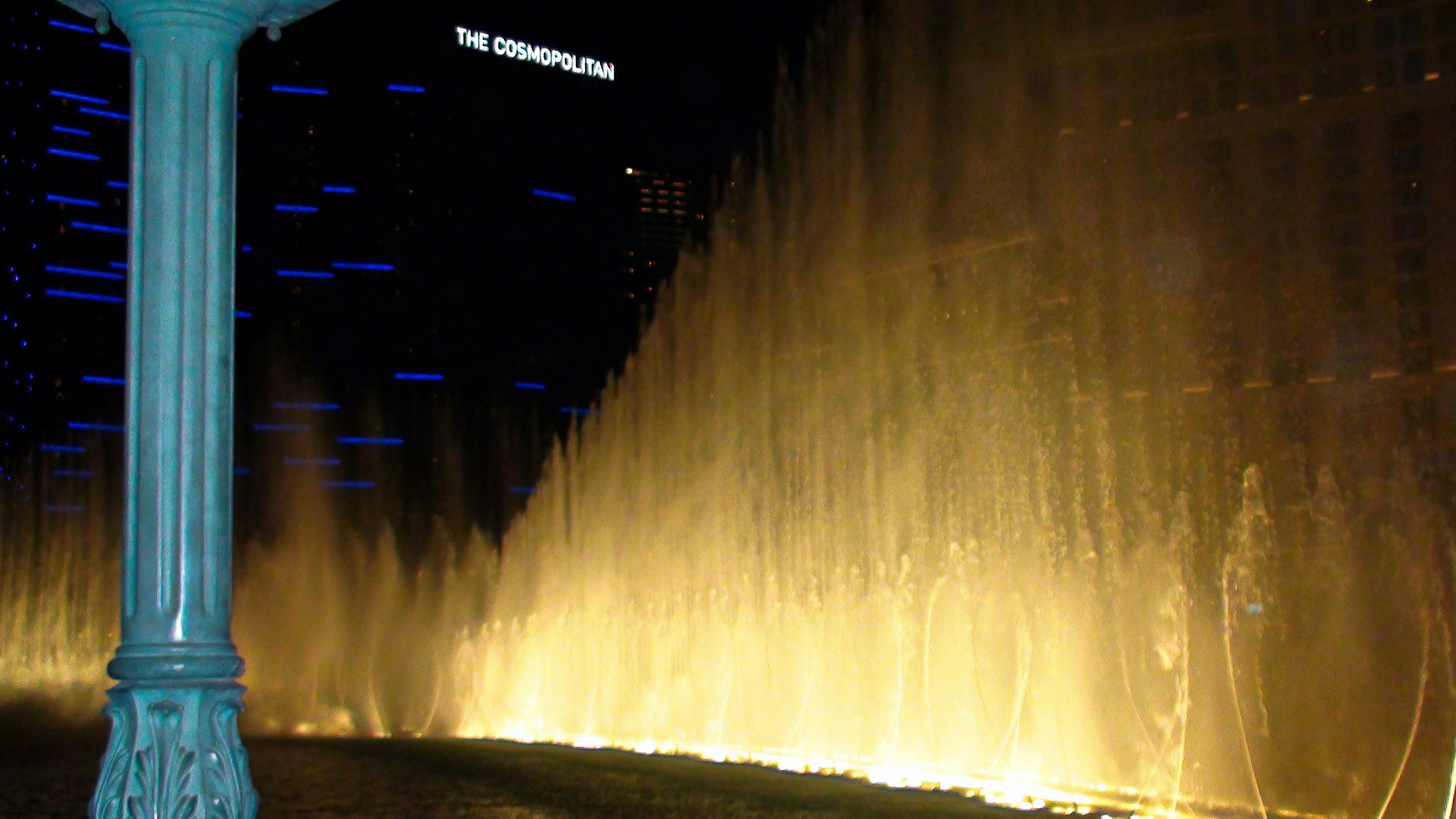 Illuminated water fountain show at night with a column.
