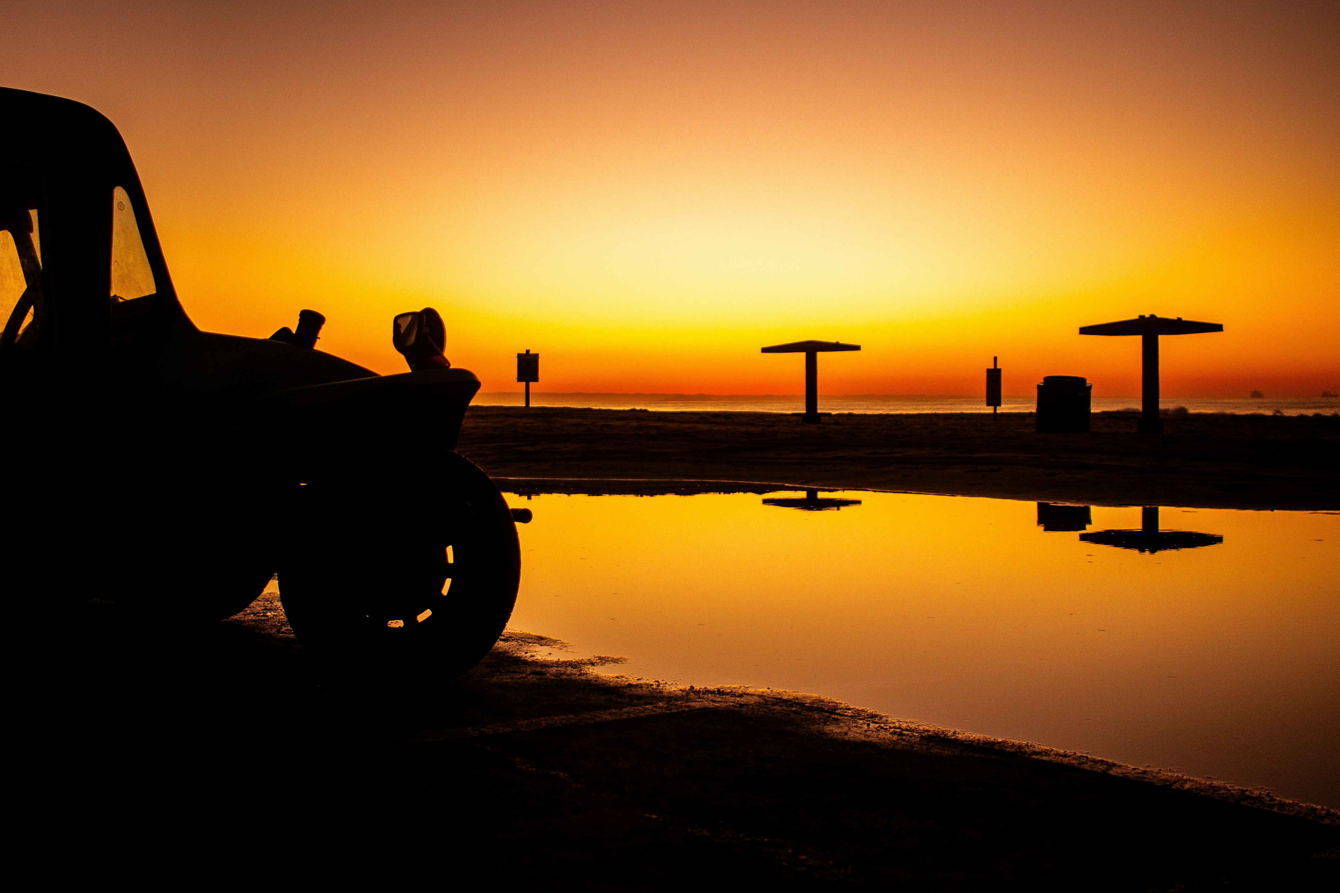 Silhouette of a vintage car on a beach at sunset