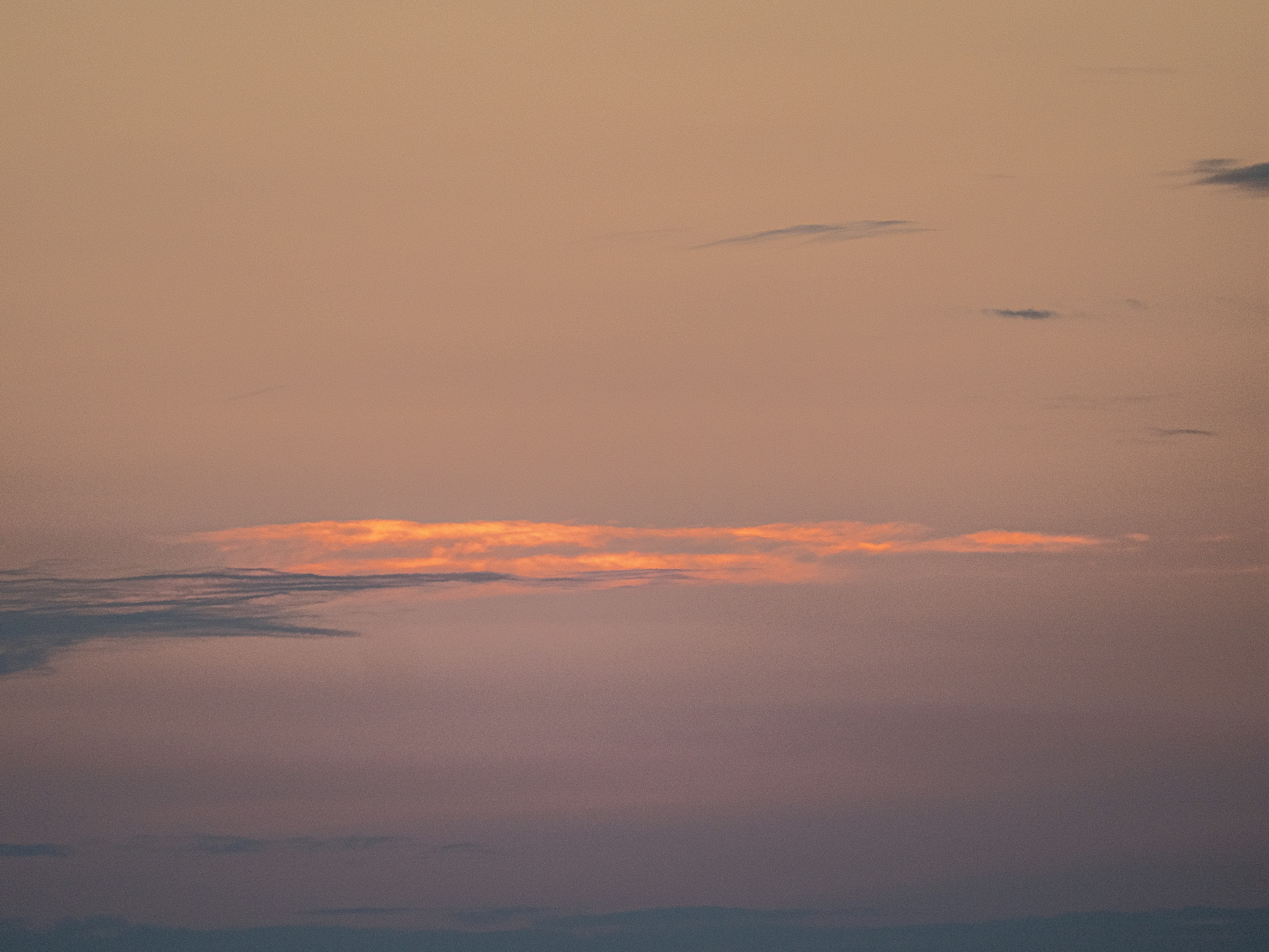 Eine lange, beleuchtete Wolke erstreckt sich über einen farbenfrohen Sonnenuntergangshimmel.