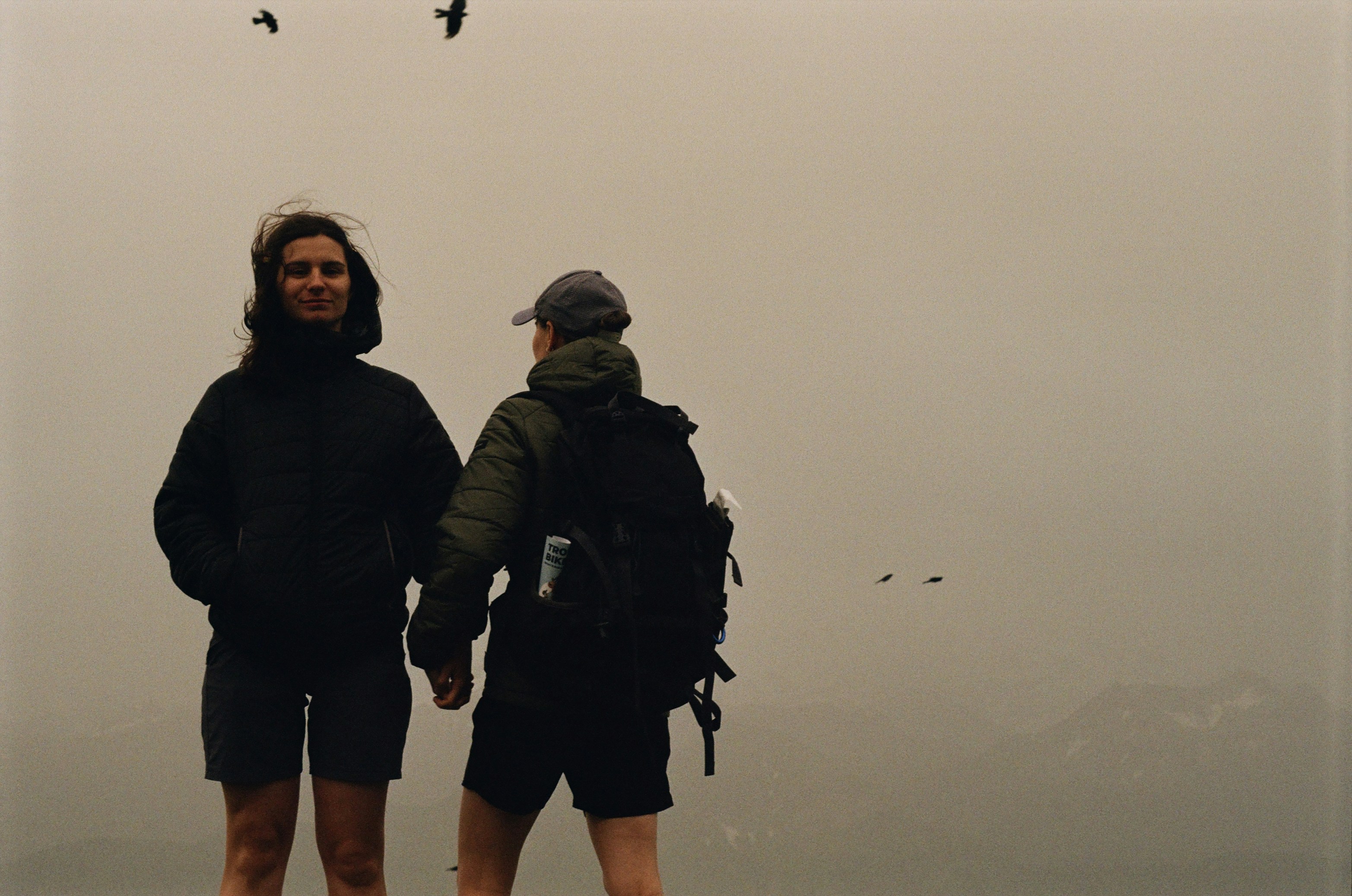 Two hikers stand in a foggy, overcast landscape