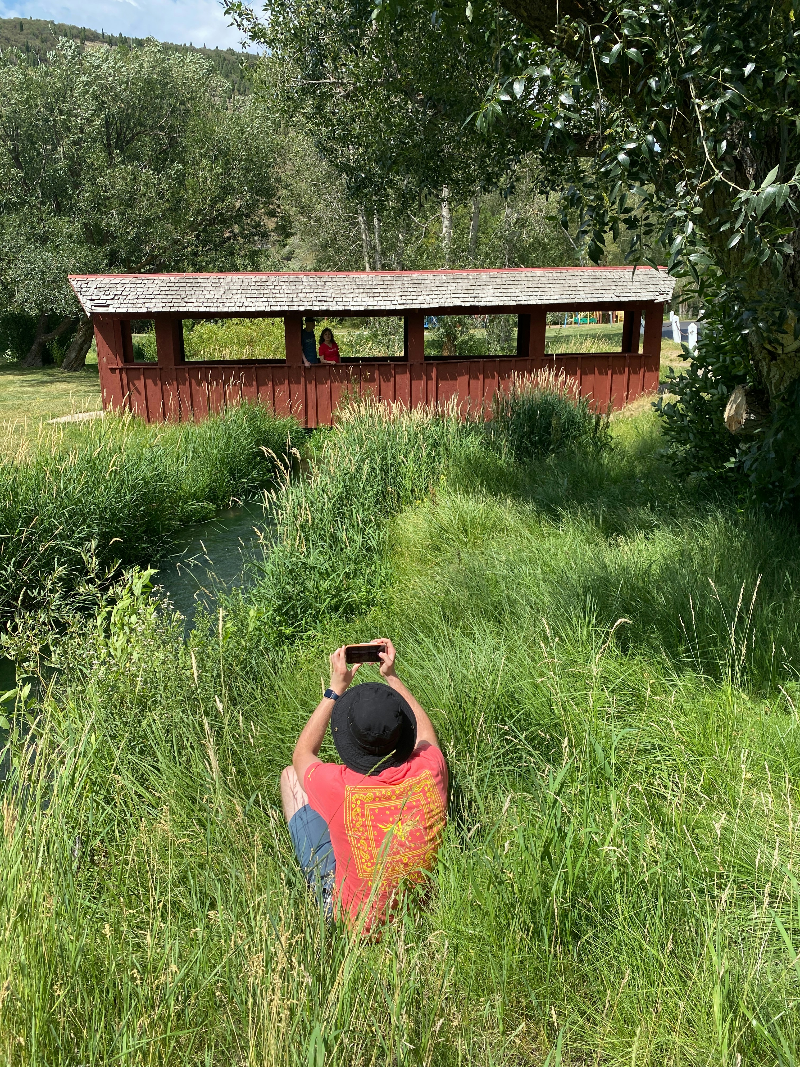 Person im hohen Gras fotografiert eine rote überdachte Brücke