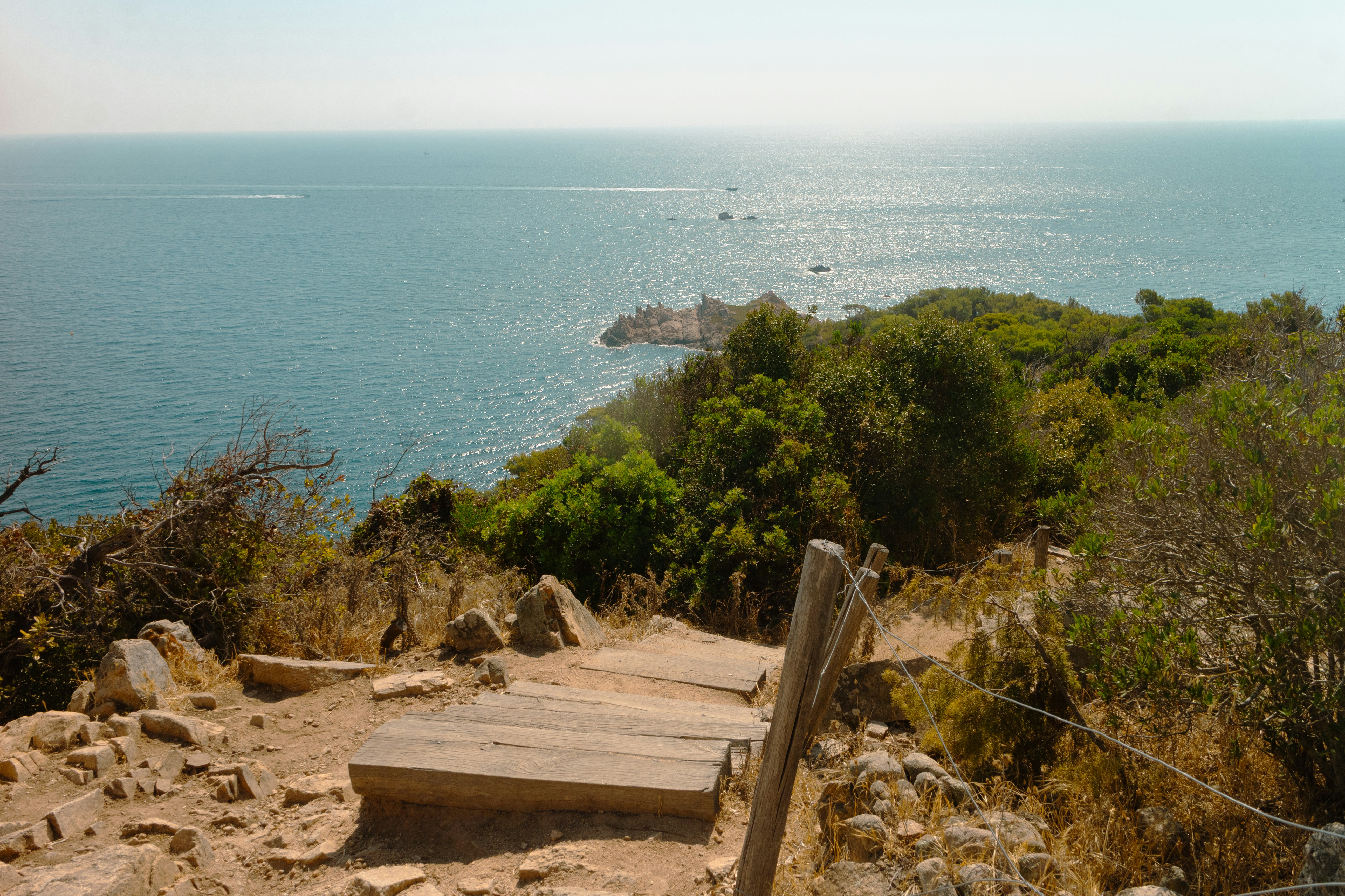 Sunny coastal path descends towards the sparkling blue ocean