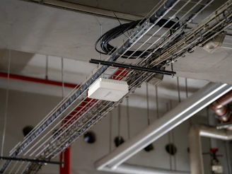 Cables, pipes, and a white box on a utility ceiling