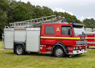 A red fire truck with ladders parked on green grass