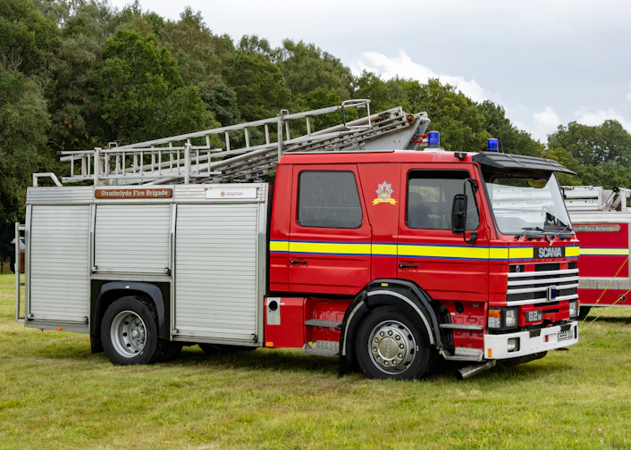 A red fire truck with ladders parked on green grass