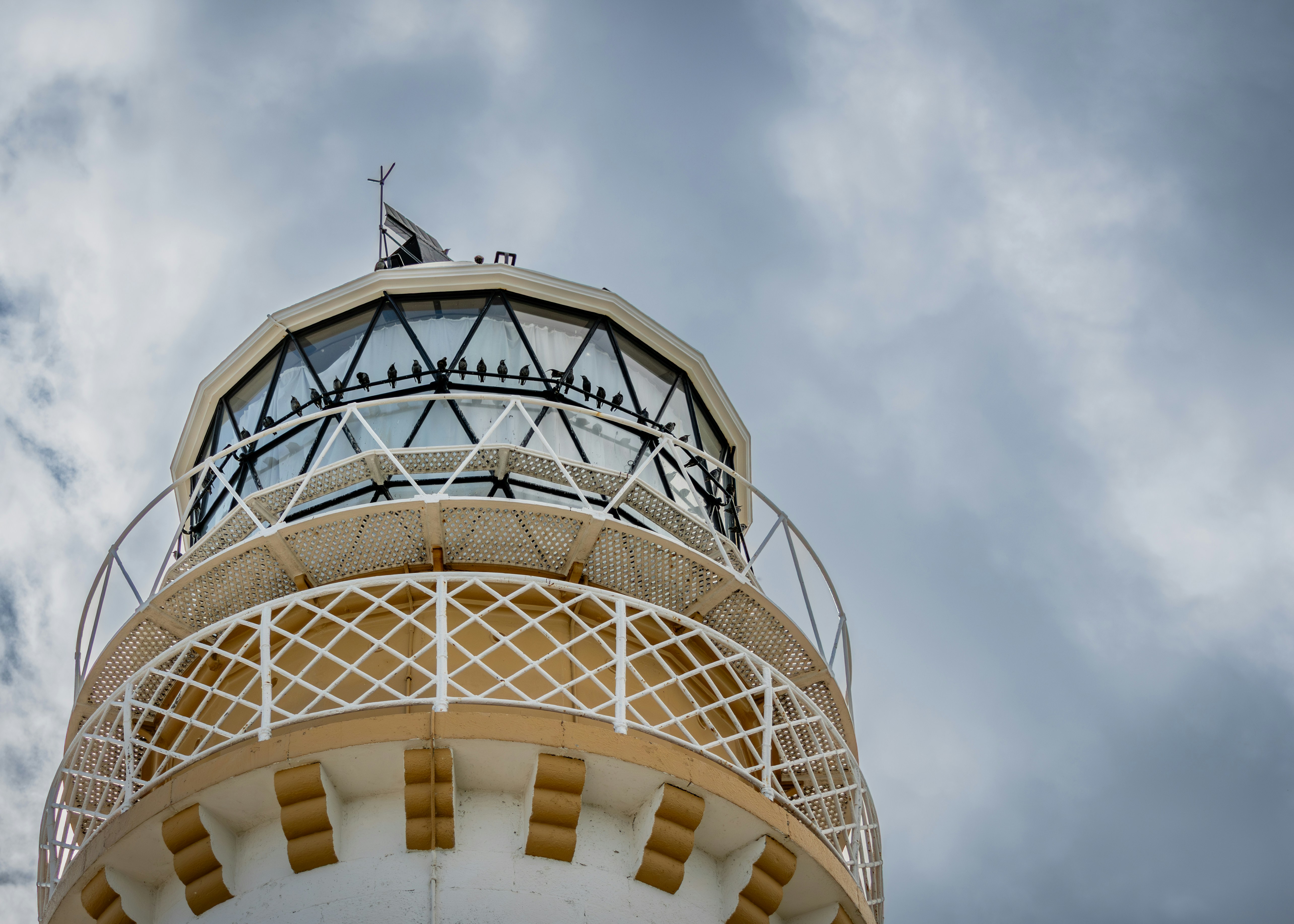 The top of a white lighthouse against a cloudy sky.