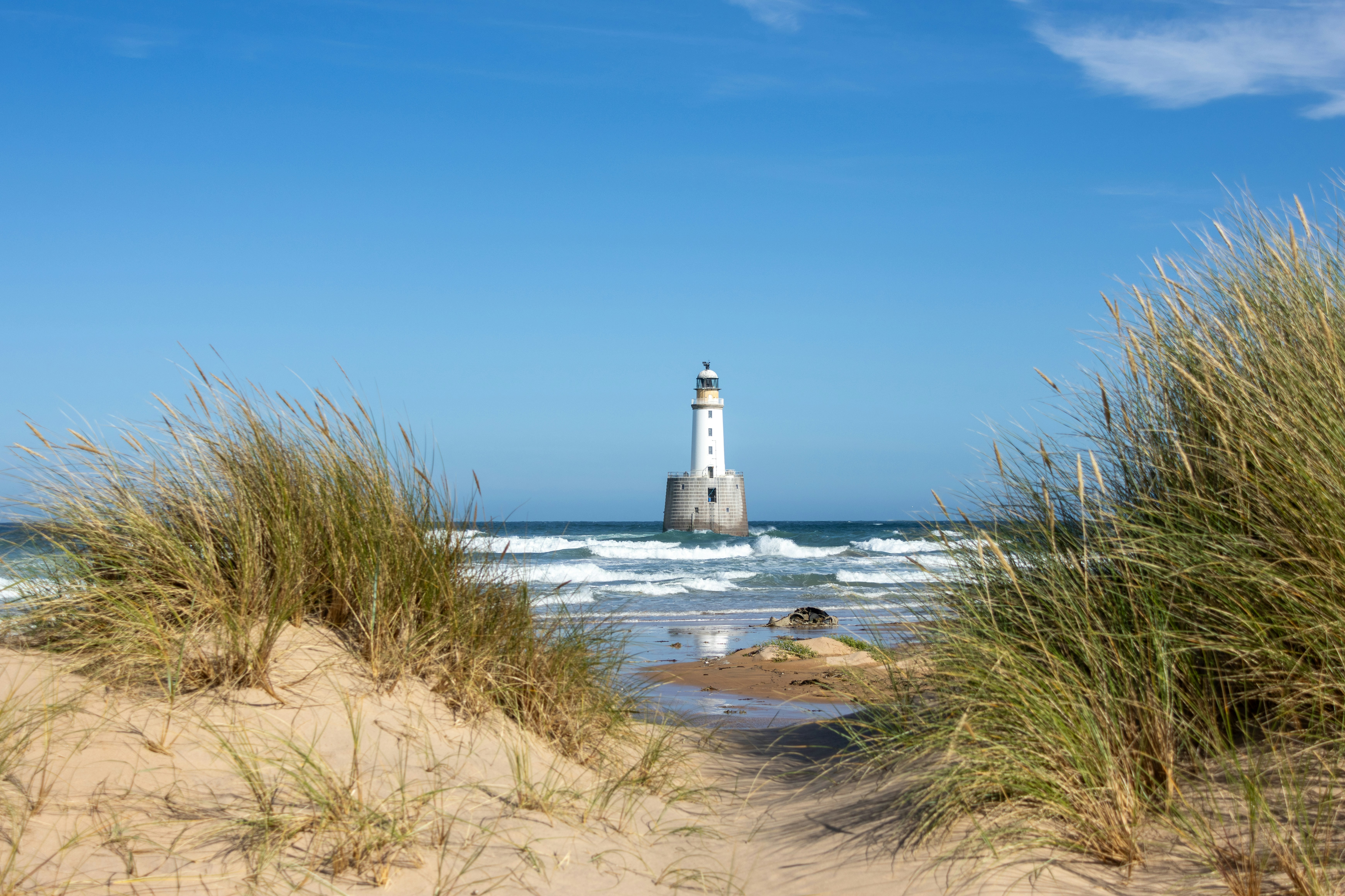 Lighthouse in the sea viewed from sandy dunes.