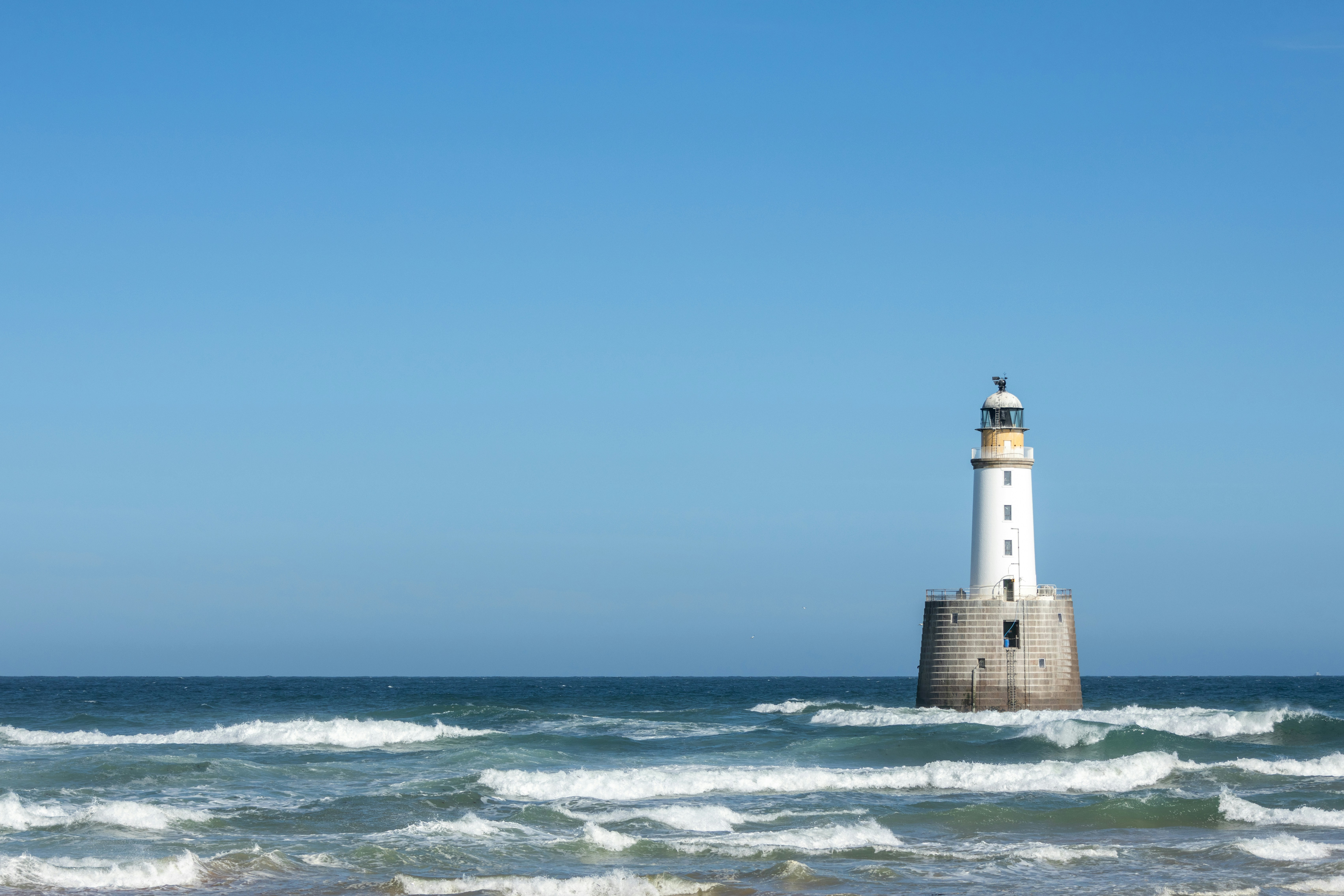 Lighthouse in the ocean under a clear blue sky.