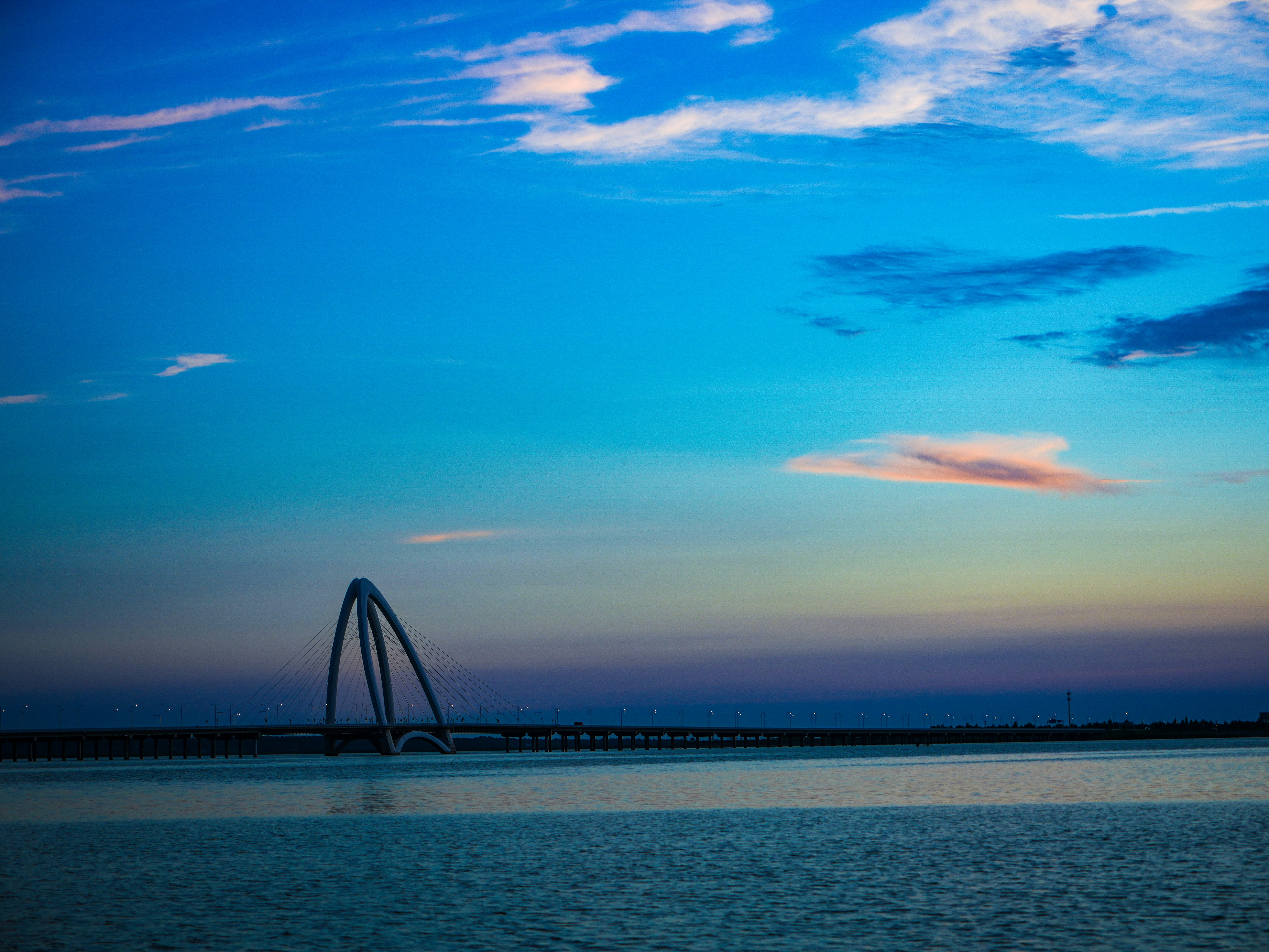 Arched bridge silhouette against twilight sky over calm water