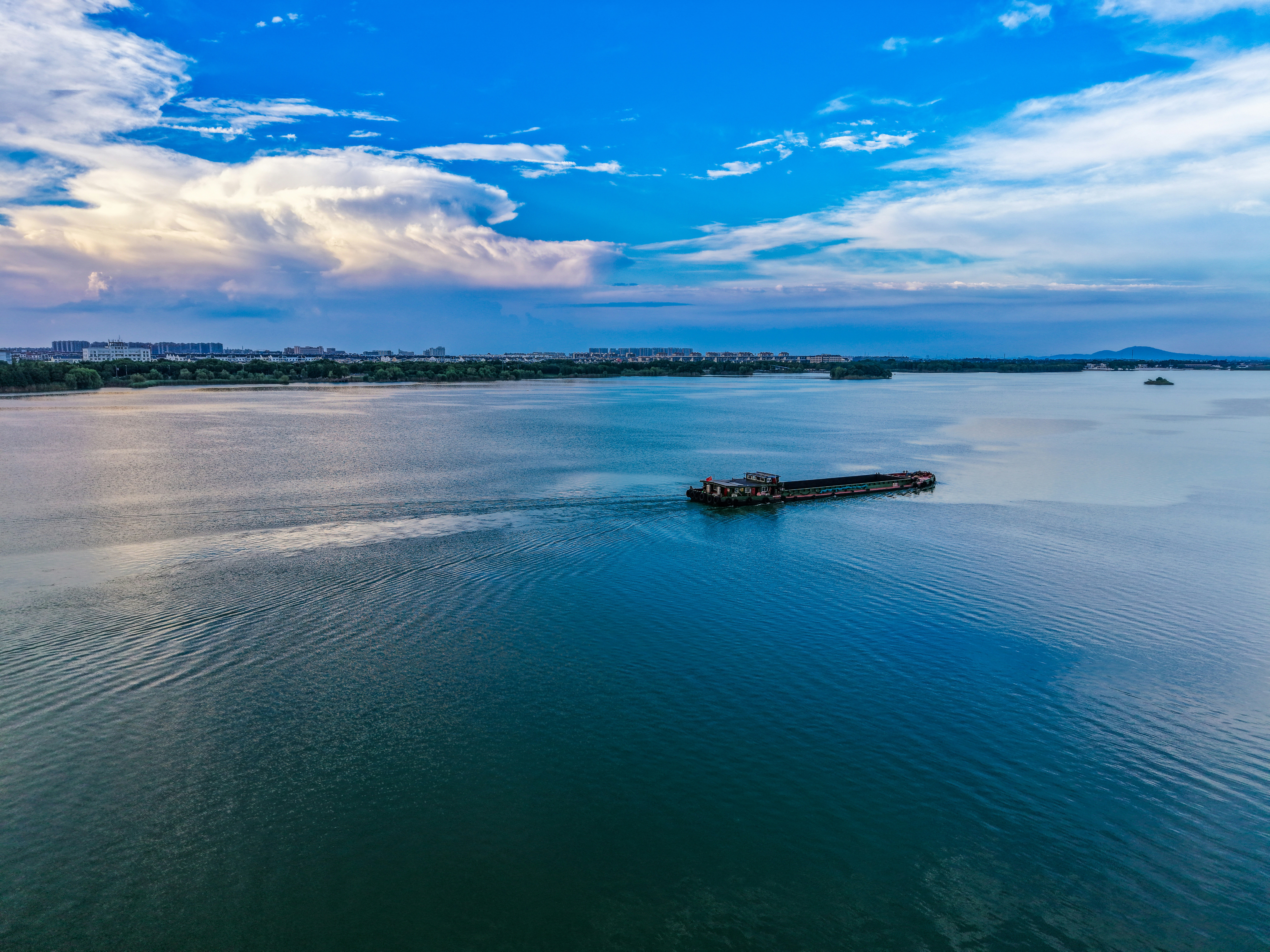 A barge navigates a wide river under a blue sky