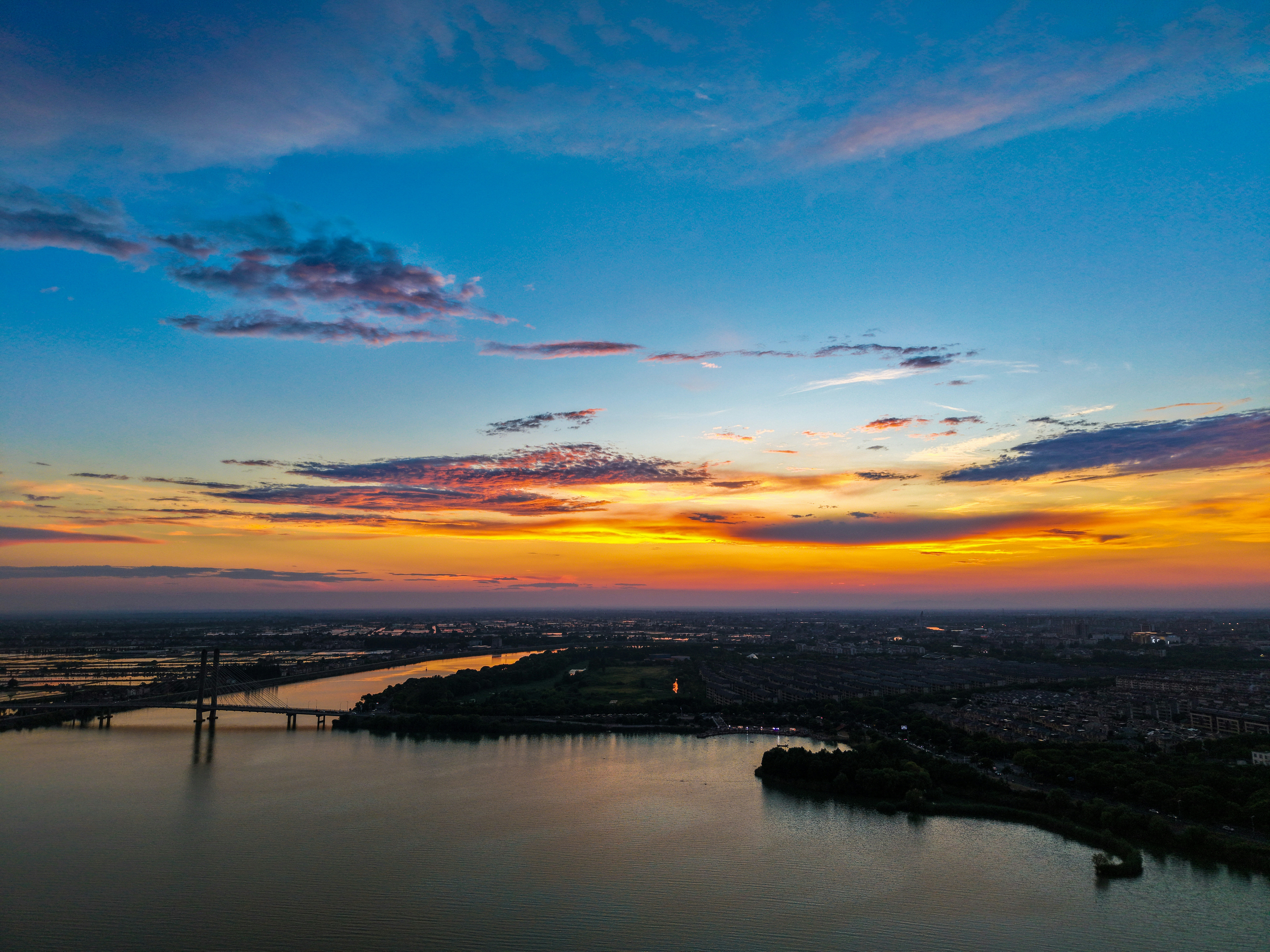 Vibrant sunset over a river, bridge, and distant city