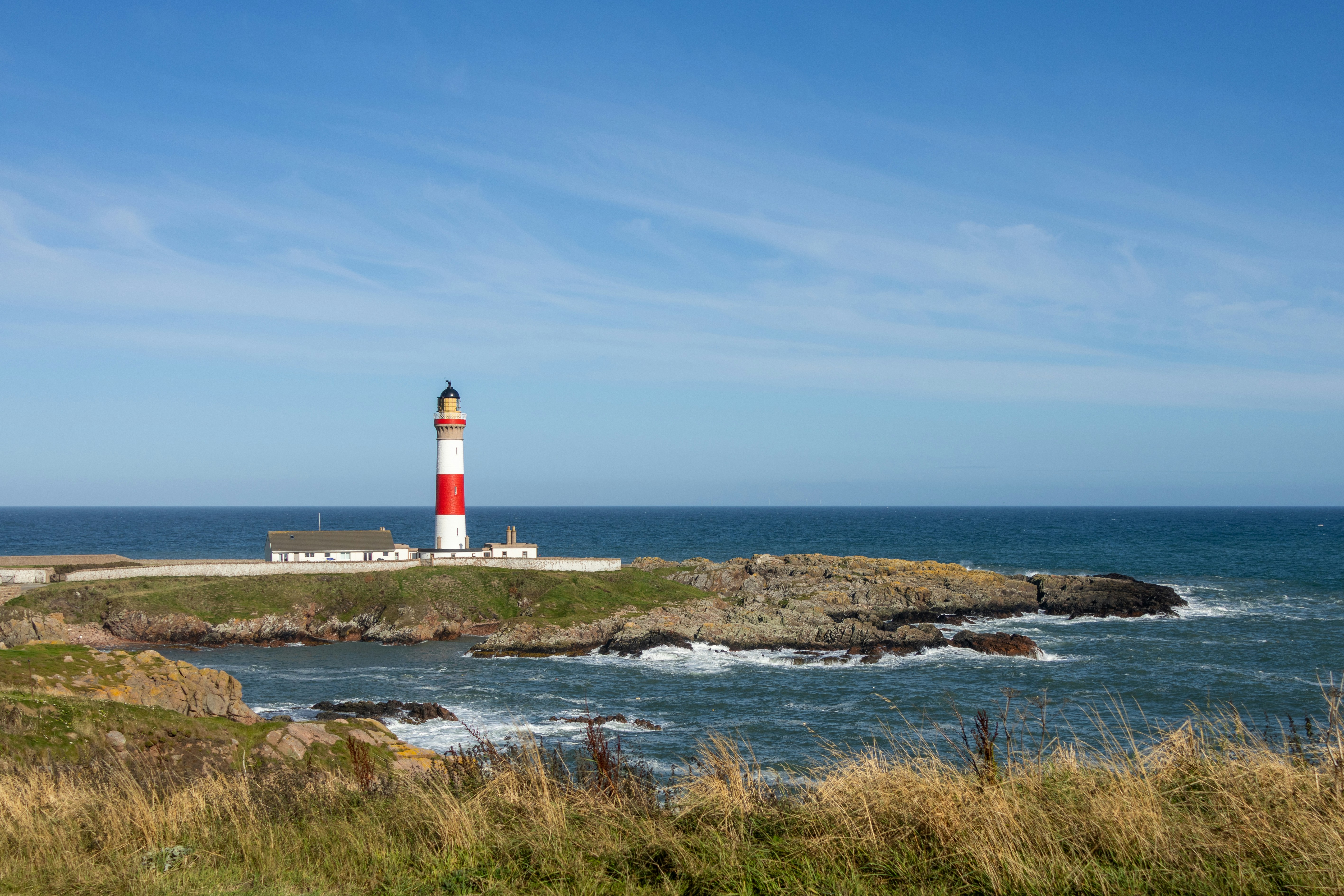 A red and white lighthouse stands on a rocky coast.