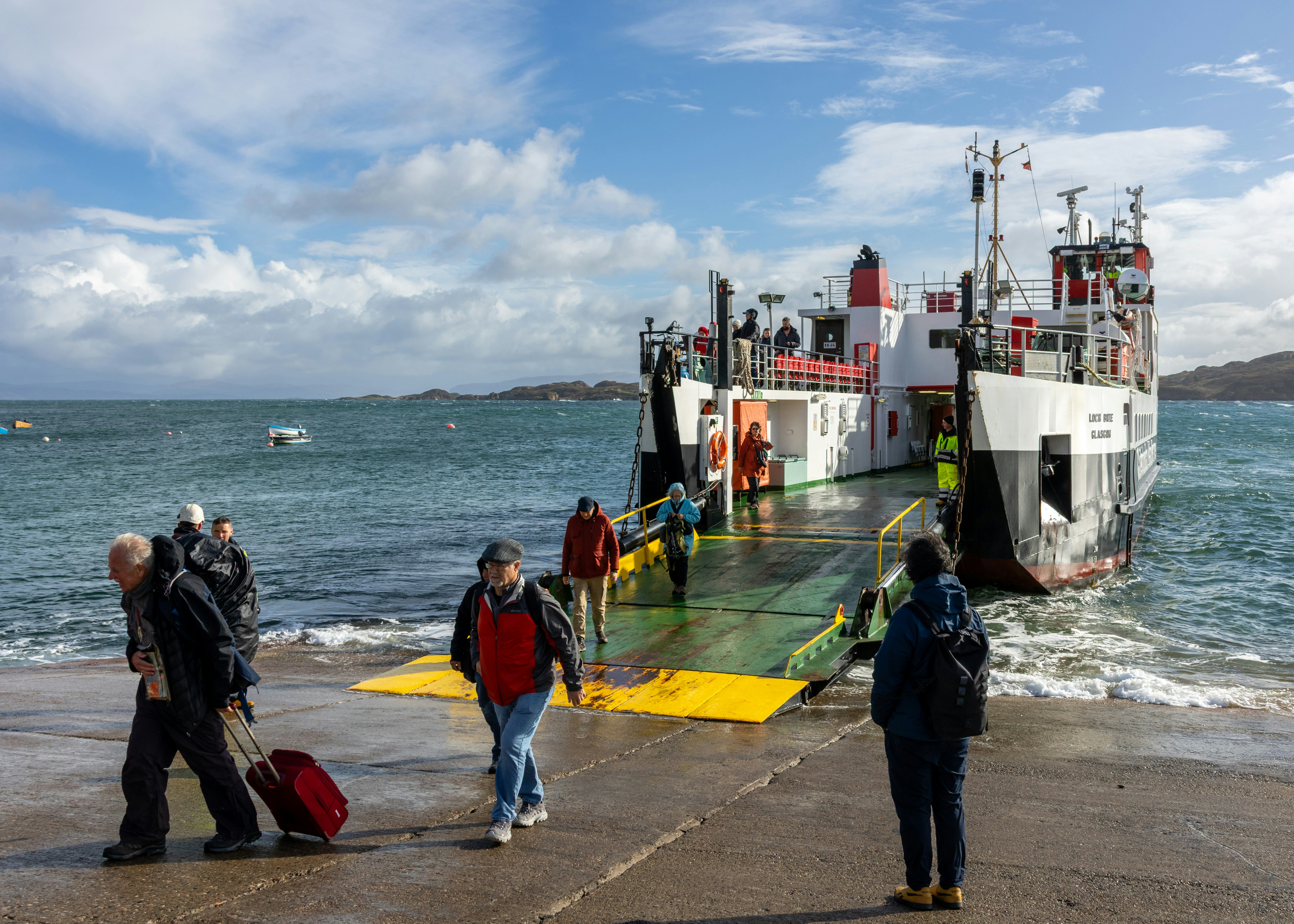 People disembarking a vehicle ferry onto a wet ramp.