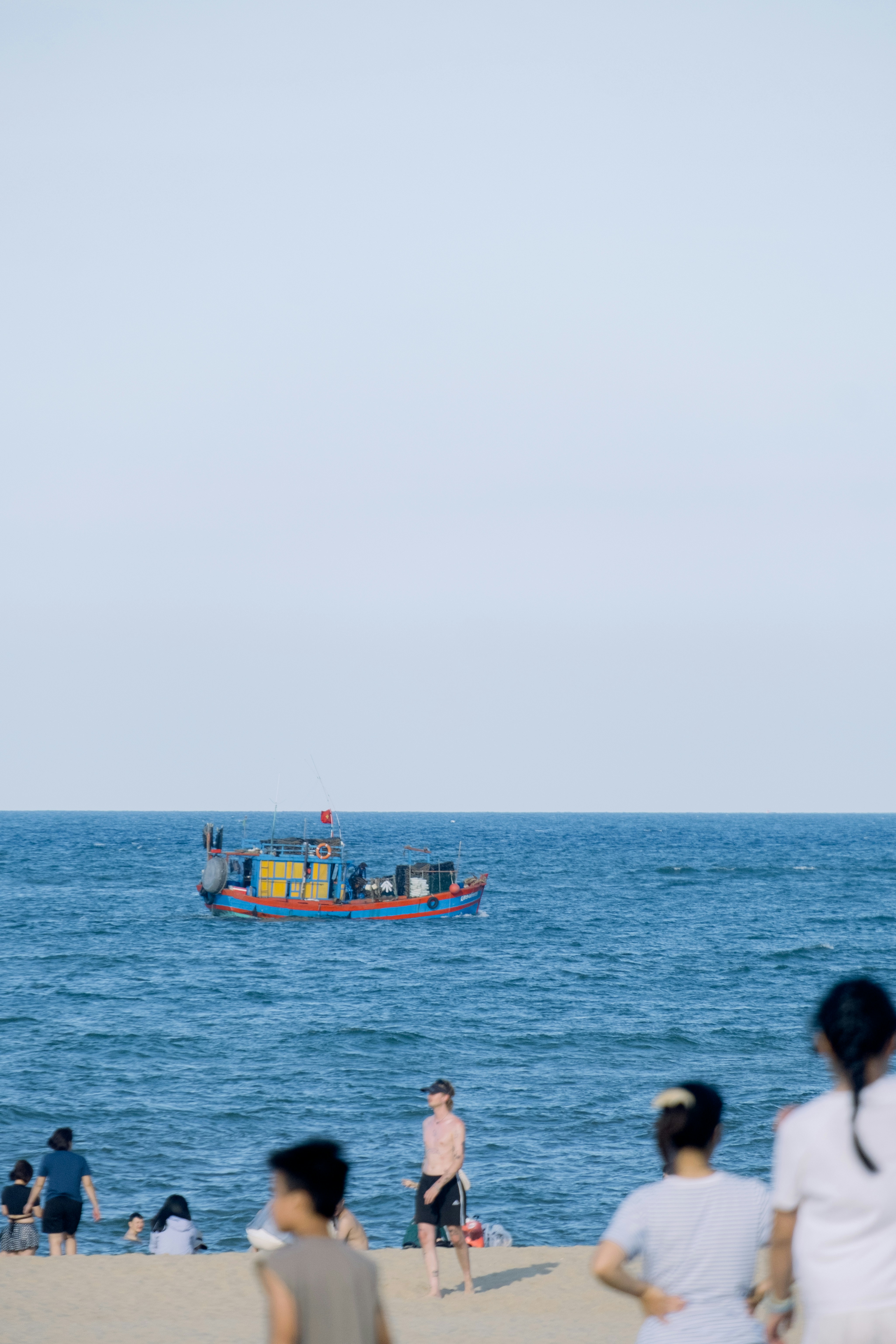 Boat on blue ocean with people relaxing on a beach.