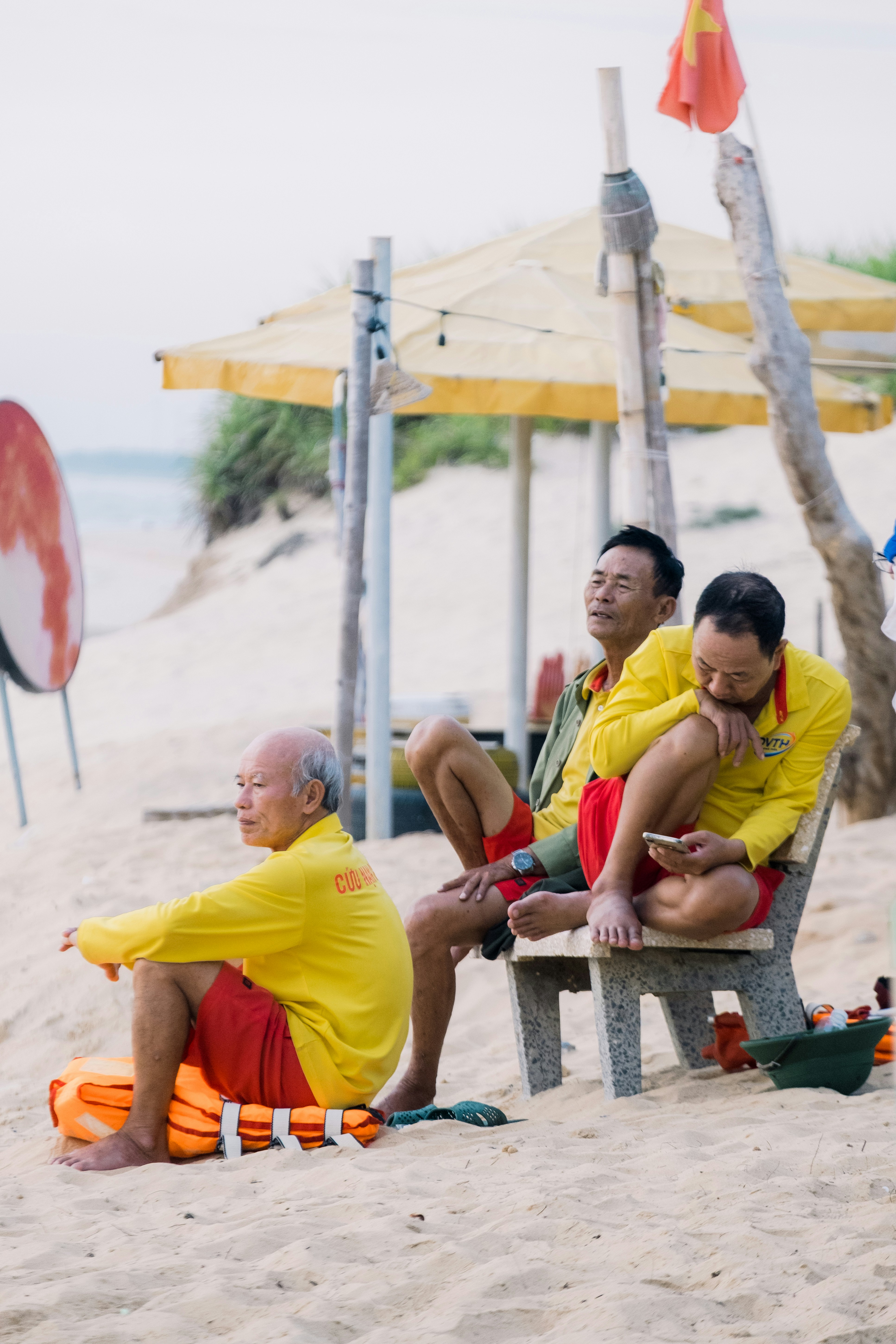 Three men in yellow shirts relaxing on a sandy beach.