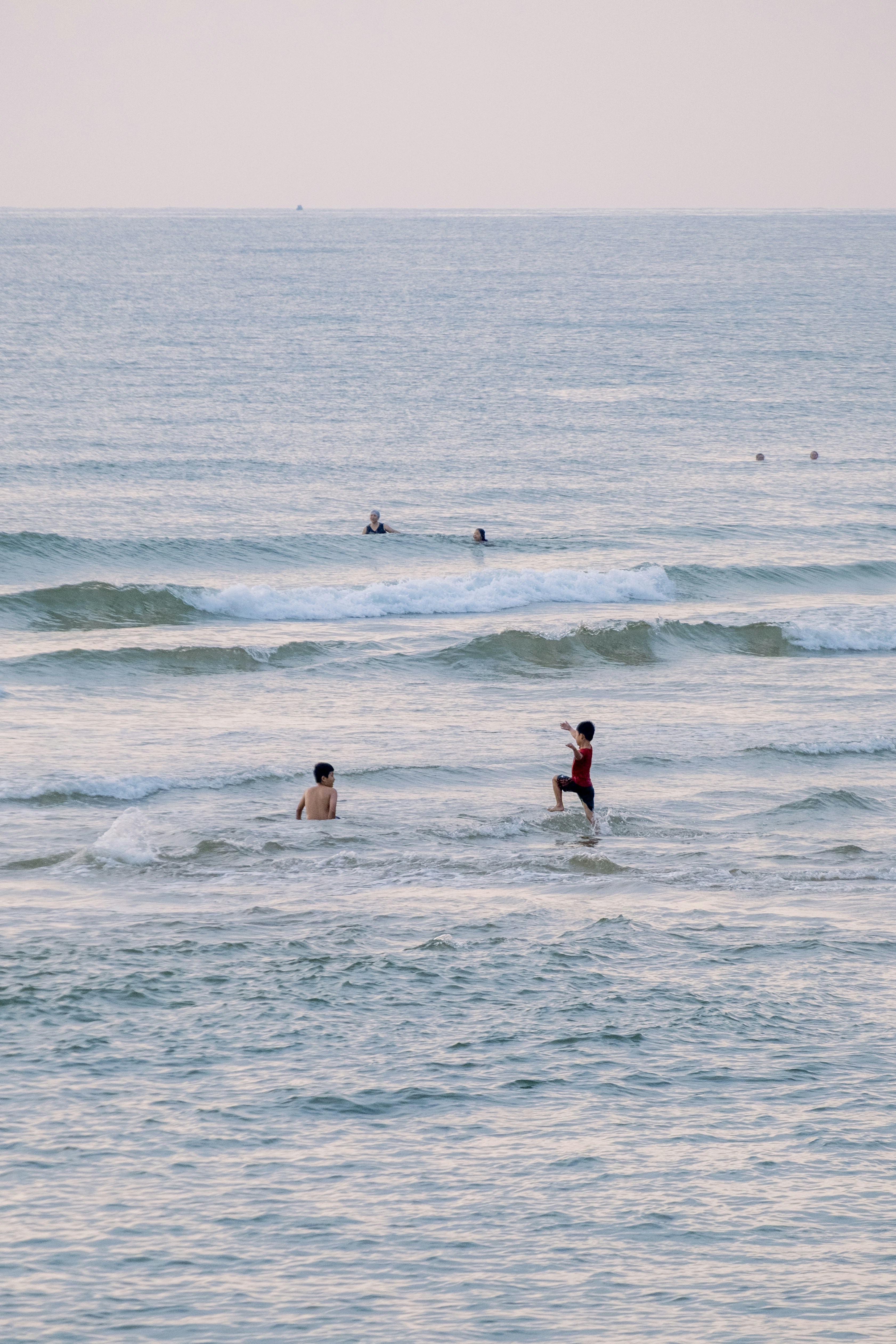 People swimming and standing in the calm ocean waves.