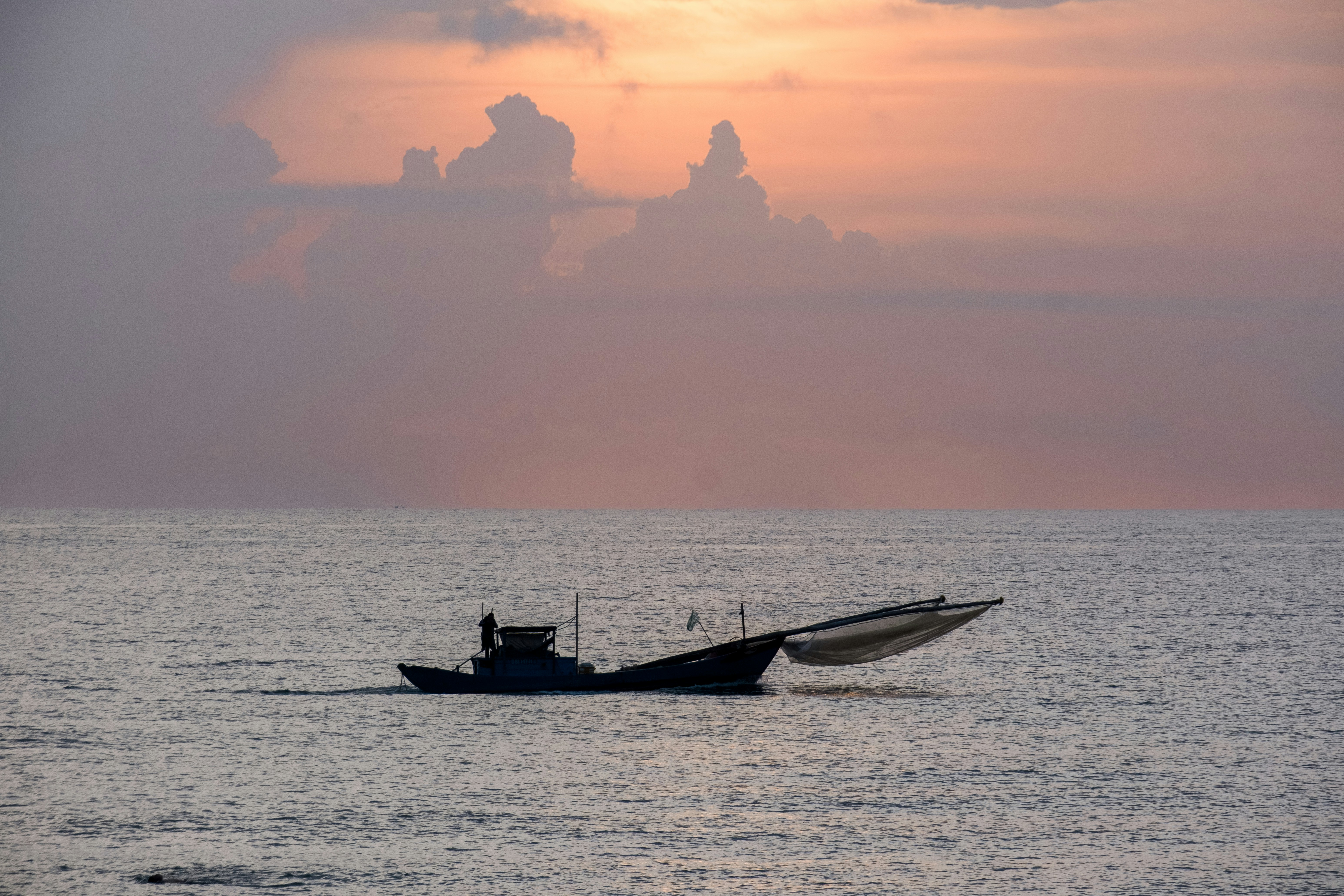 Fishing boat sailing on calm water under a sunset sky.