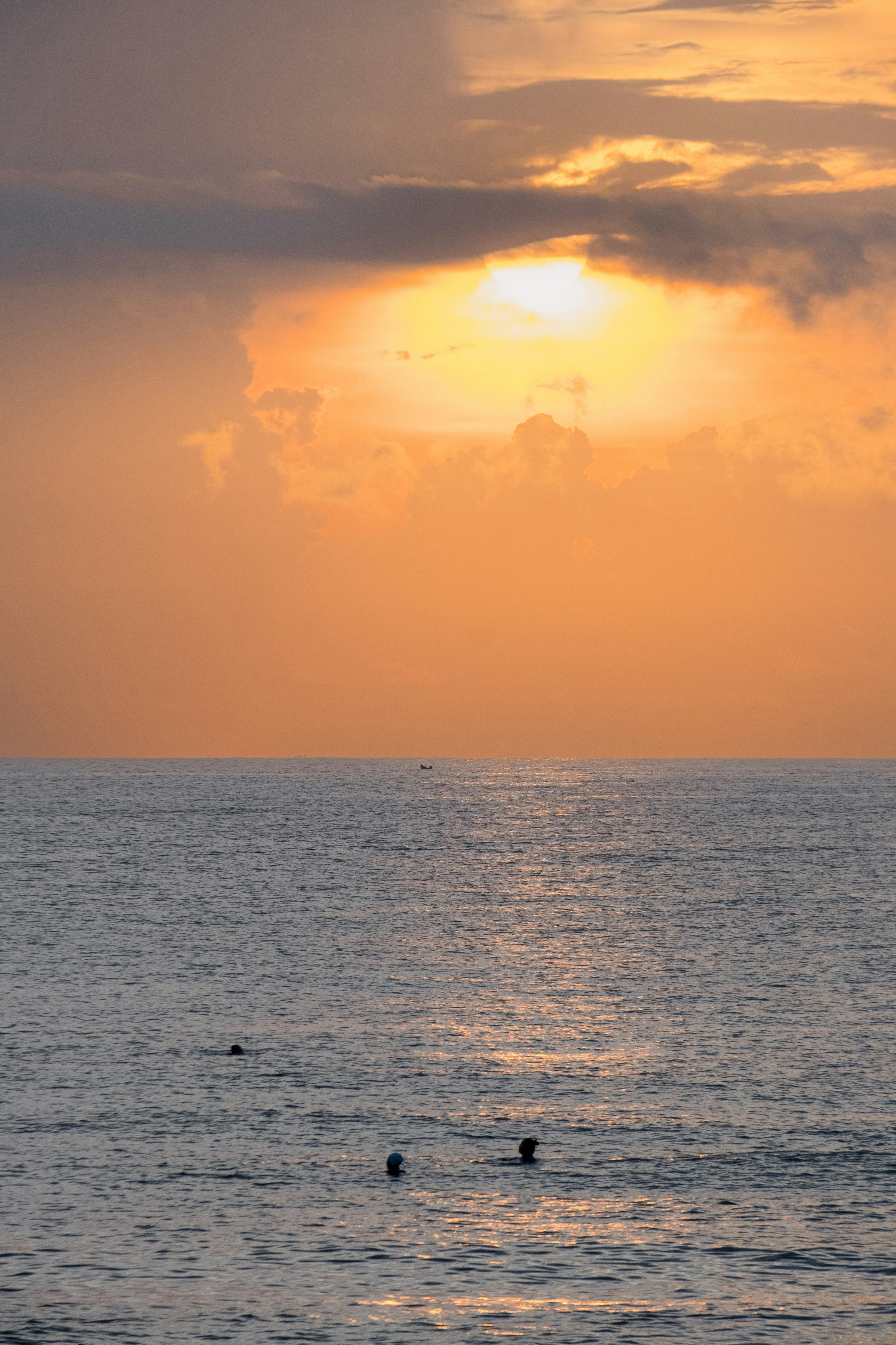 People swimming in the ocean during a vibrant orange sunset.