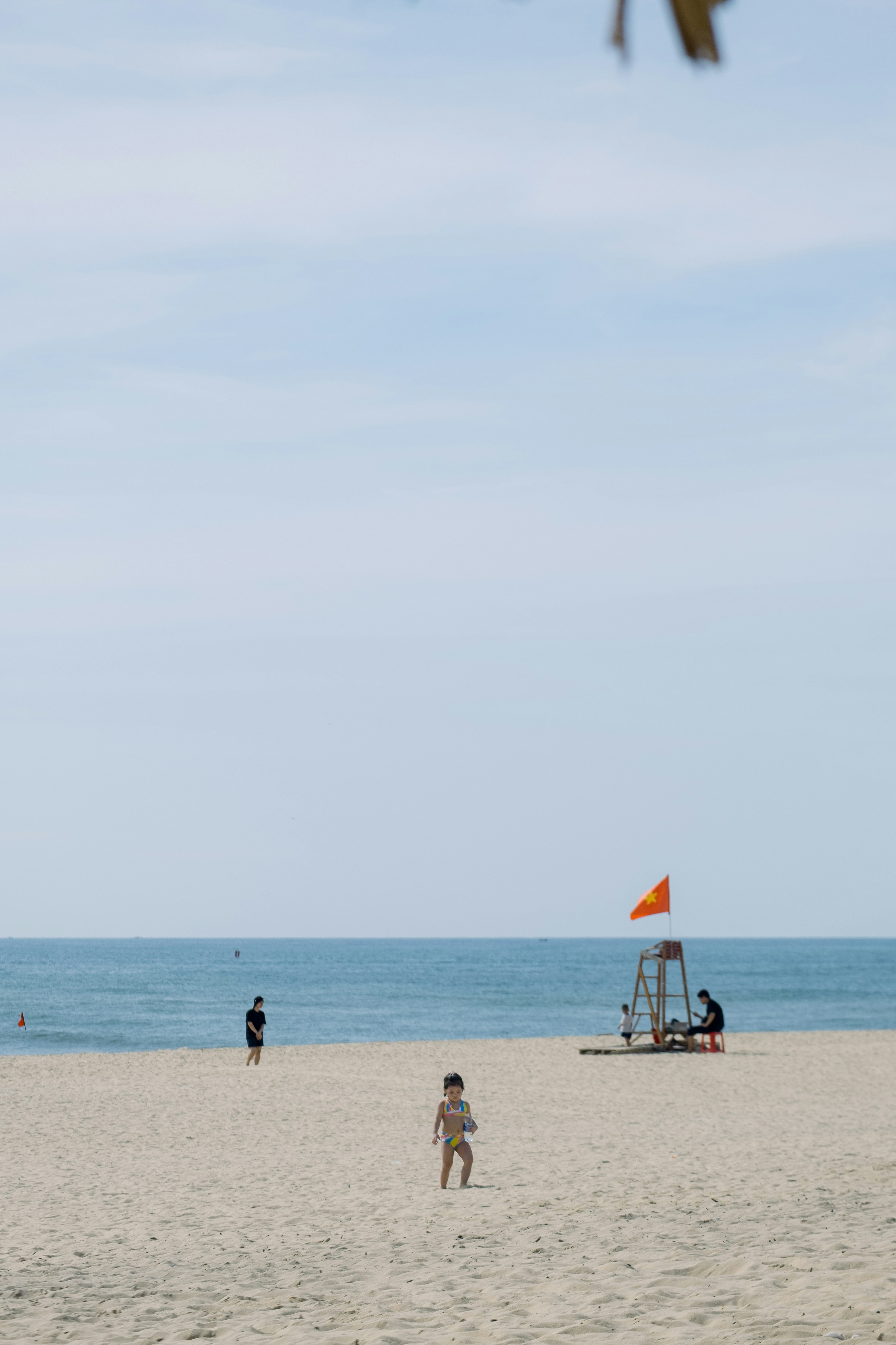 Child on a sunny beach with ocean and lifeguard stand.