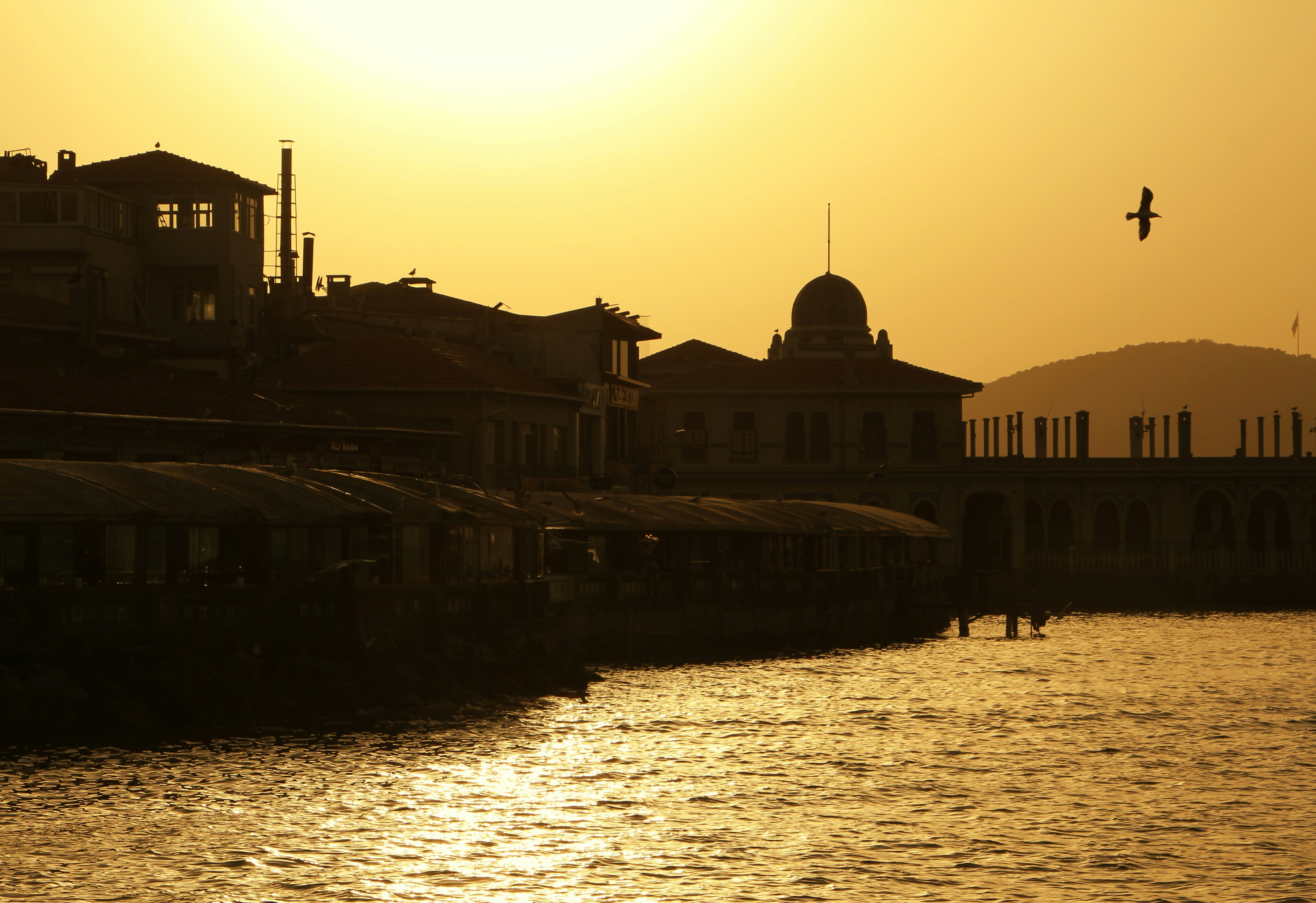 Sunset over harbor with silhouetted buildings and boats.