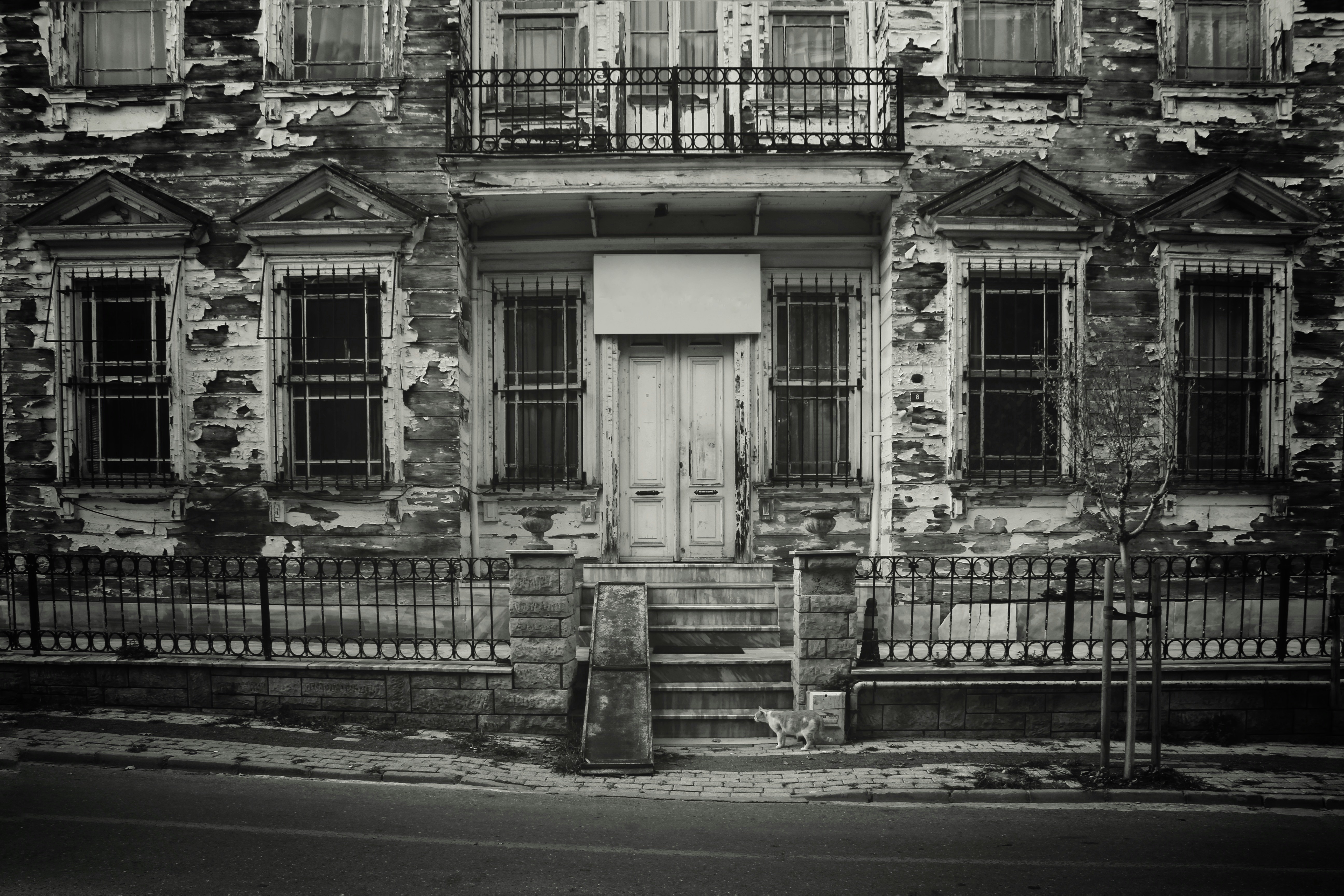 Dilapidated building facade with barred windows and central entrance.