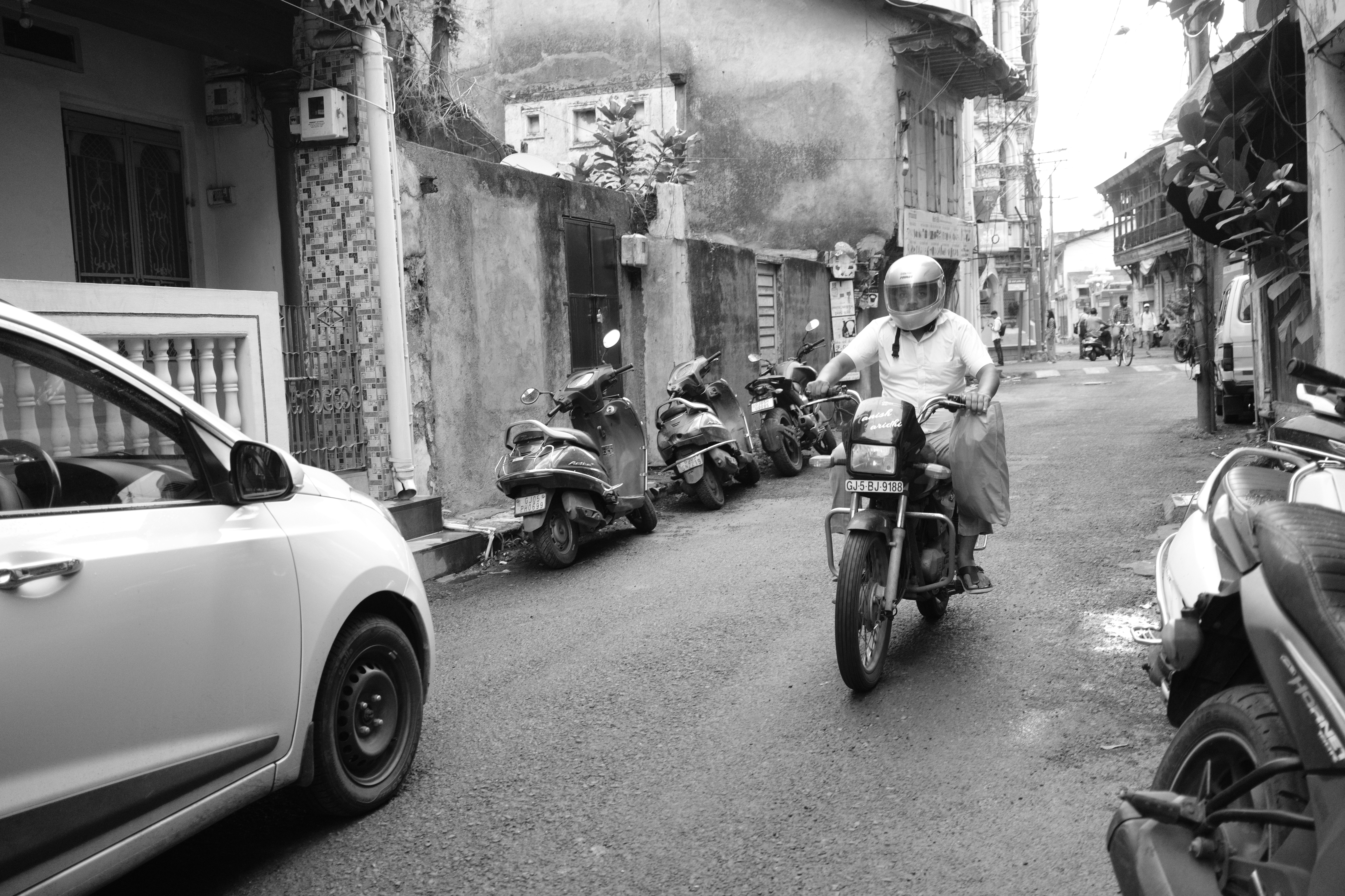 Man riding motorcycle past parked bikes on a narrow street