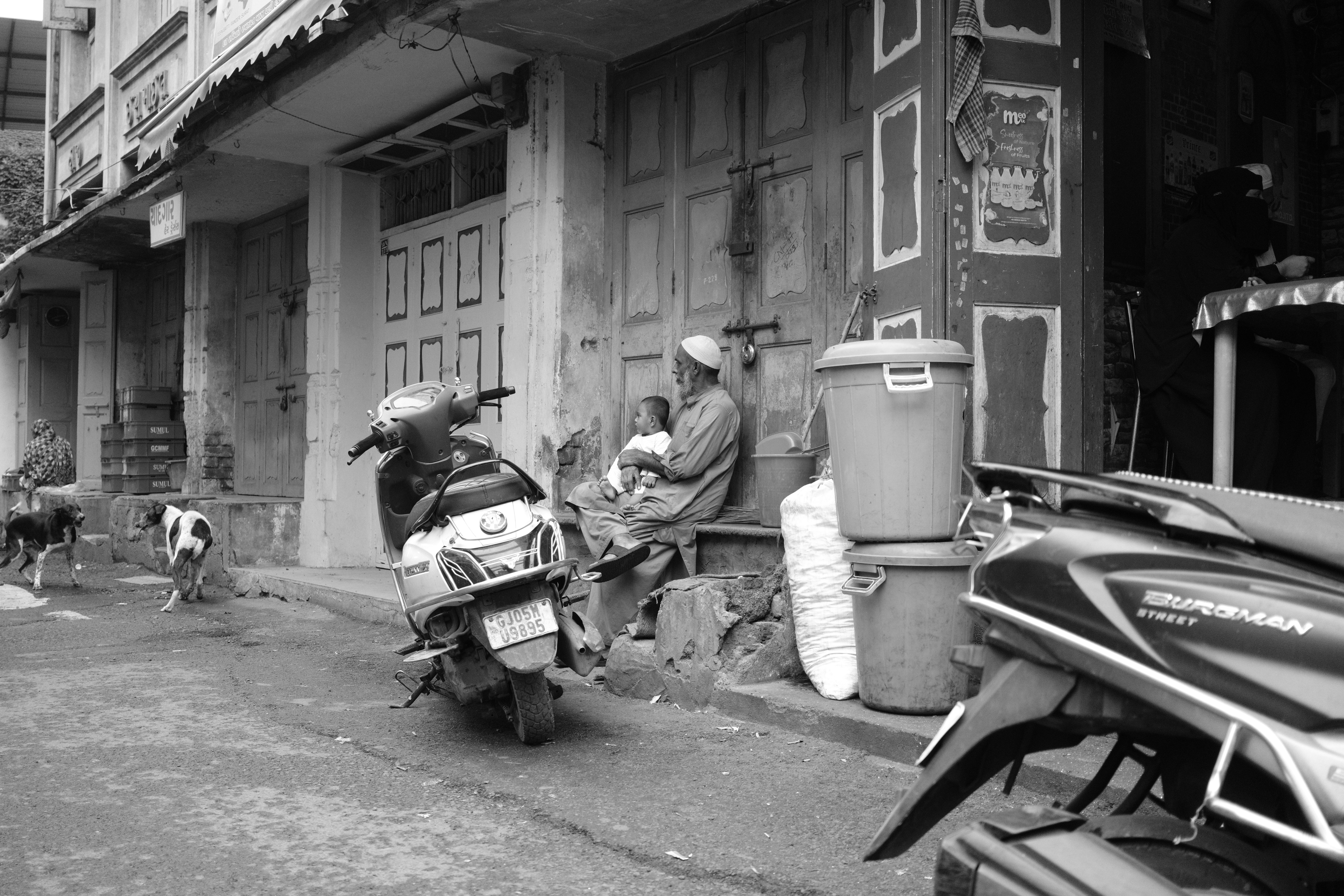 Man cradles child on urban street lined with scooters