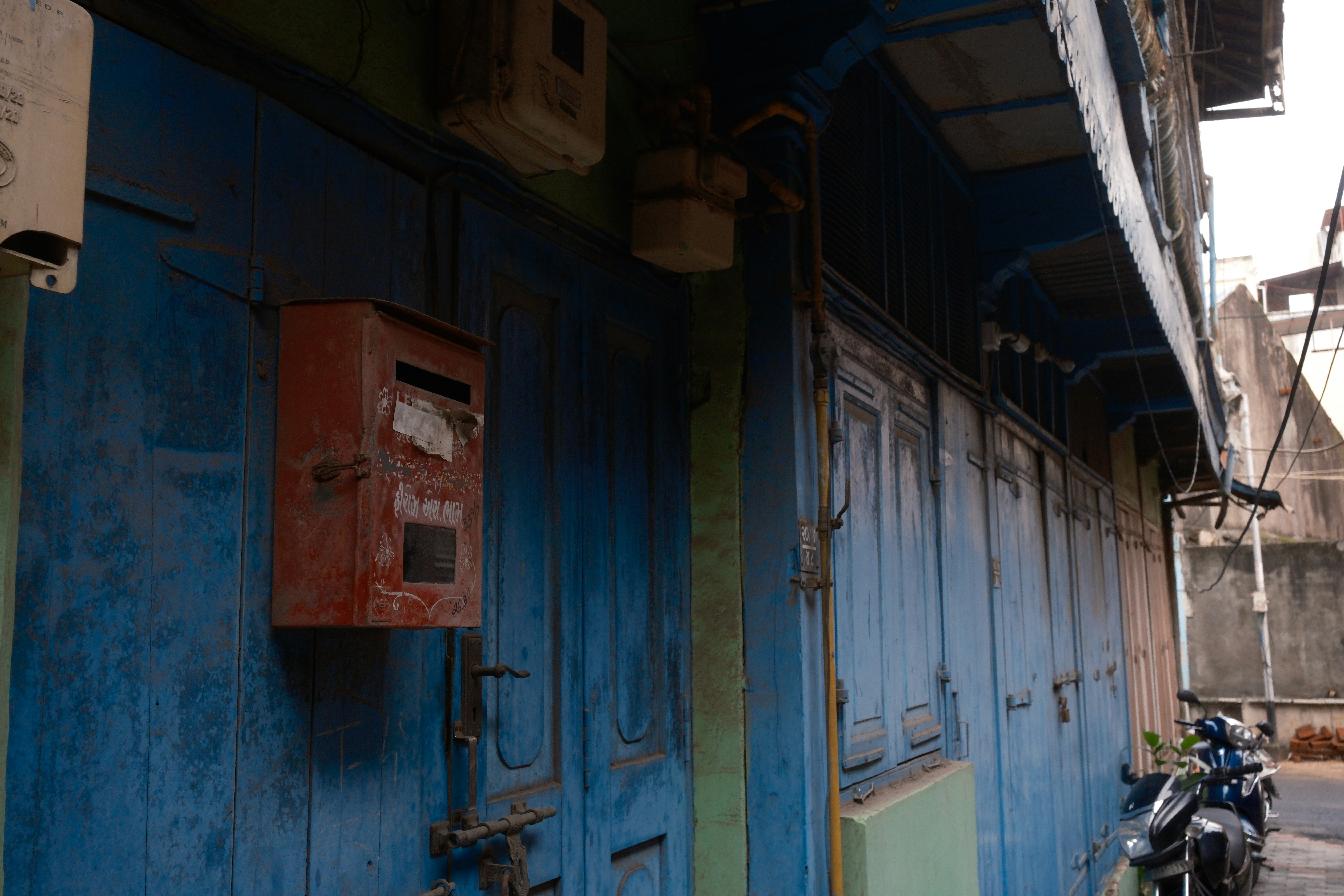 A red mailbox hangs on a weathered blue wooden shopfront