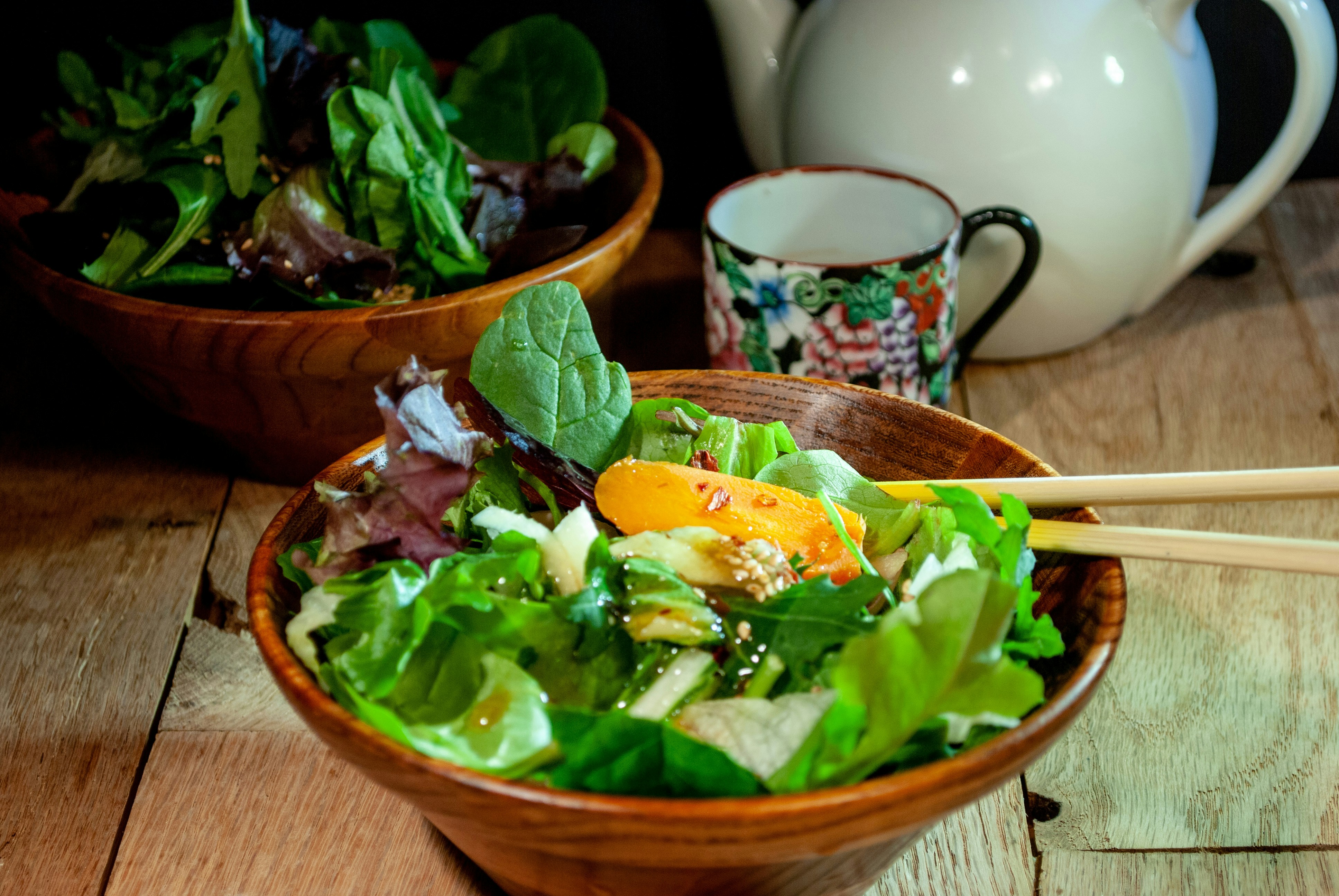 Frischer grüner Salat mit Essstäbchen, eine Teekanne und eine Tasse.