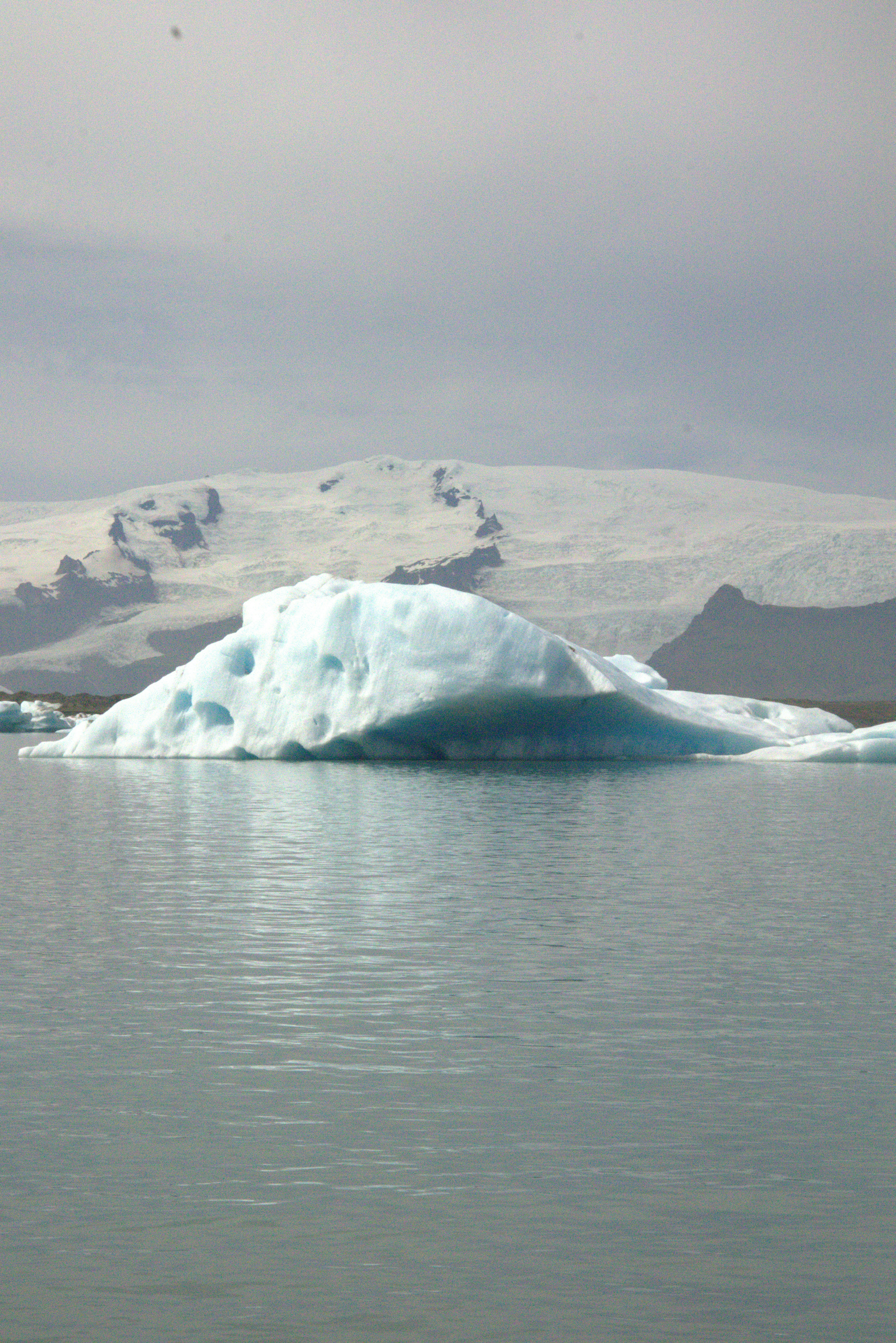 A large blue iceberg floats in water with snowy mountains - Free Photo ...