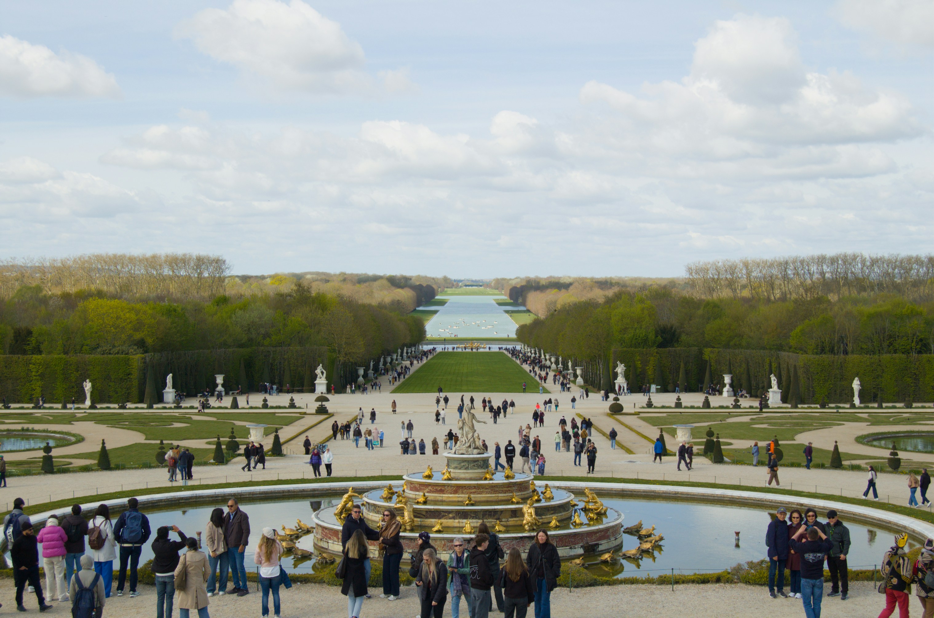 People explore a vast formal garden with a golden fountain