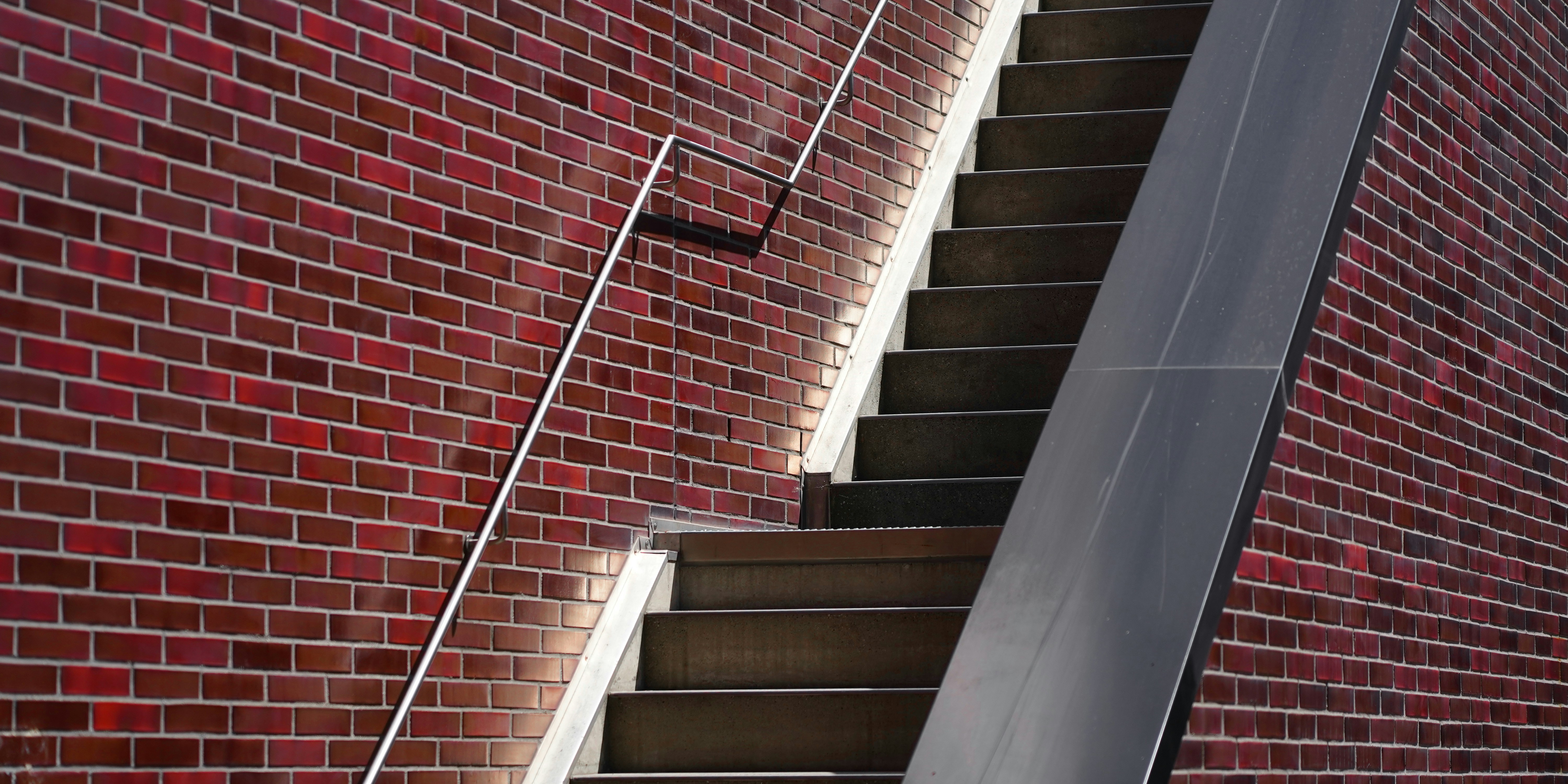 An outdoor staircase ascends alongside a red brick wall.