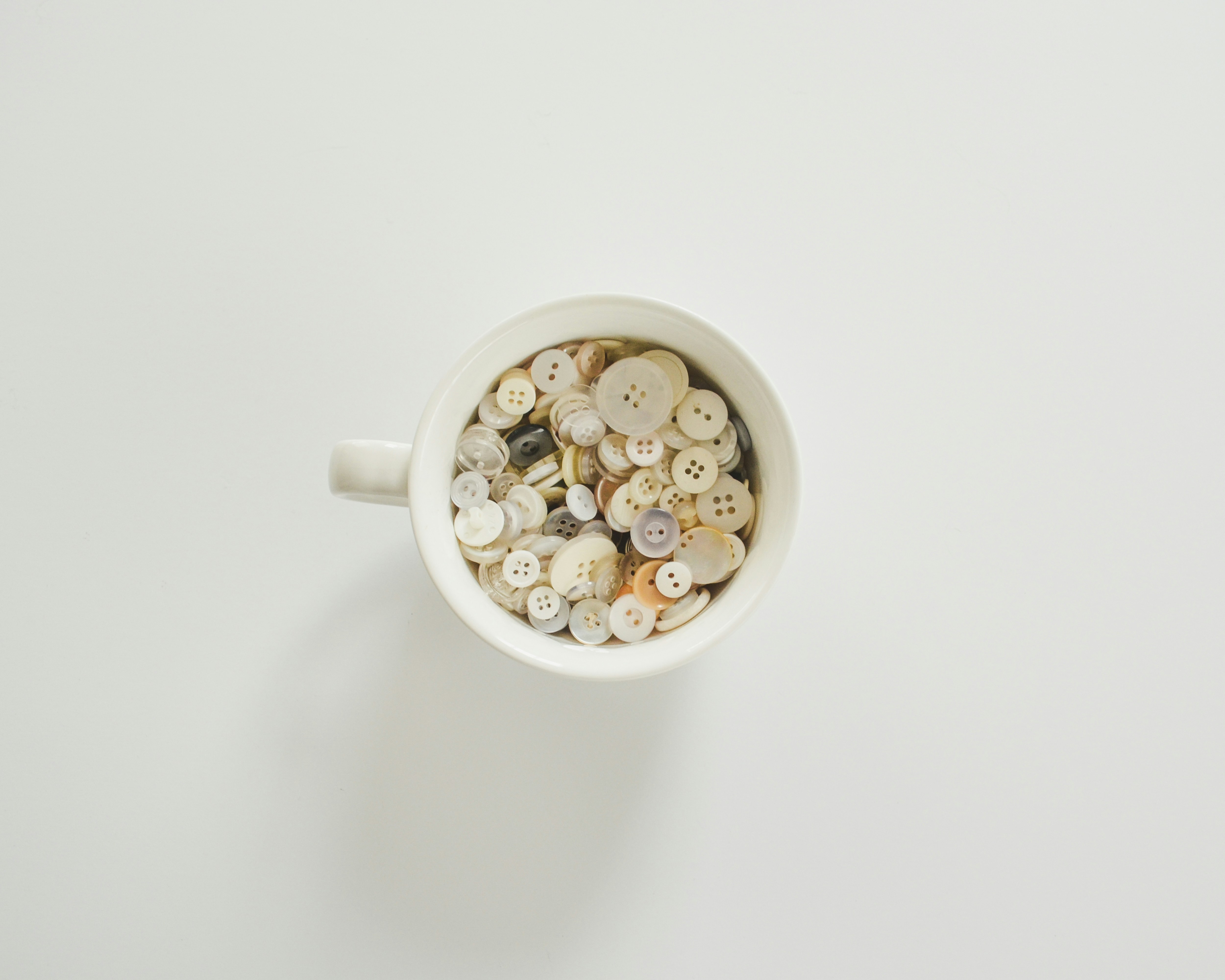 White mug filled with assorted white and beige buttons.