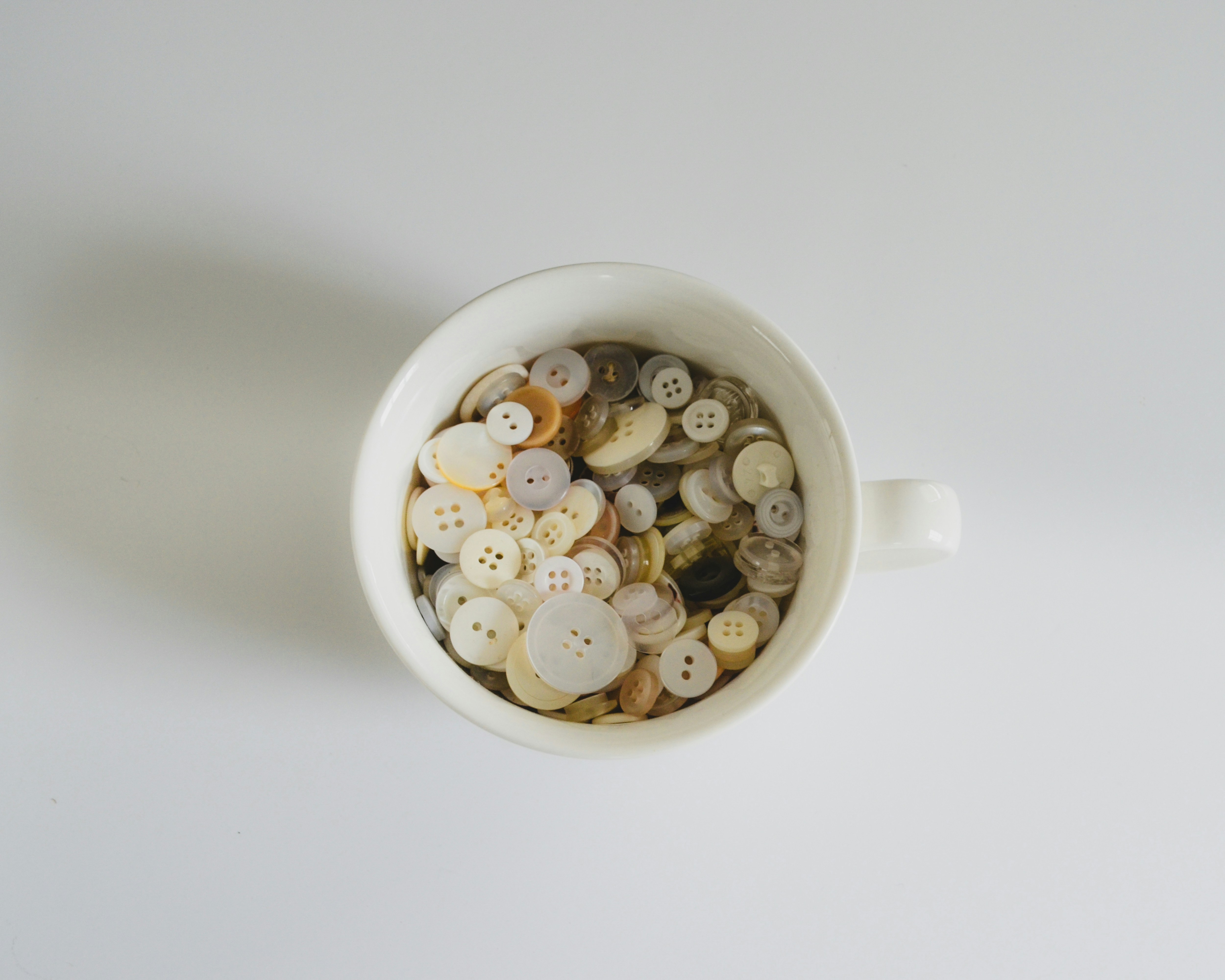 A white mug filled with assorted light-colored buttons.