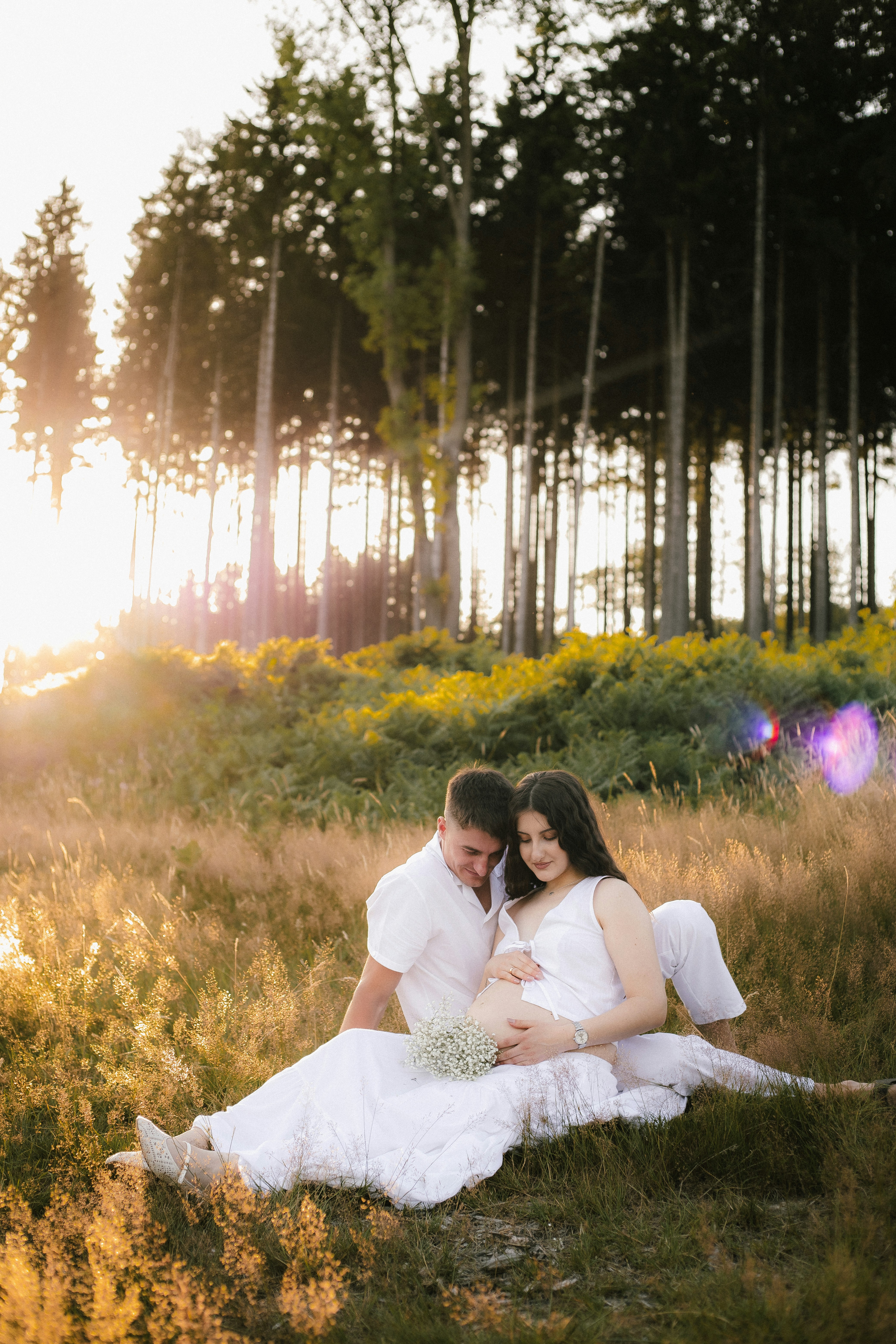 Pregnant couple sitting in a grassy field at sunset.