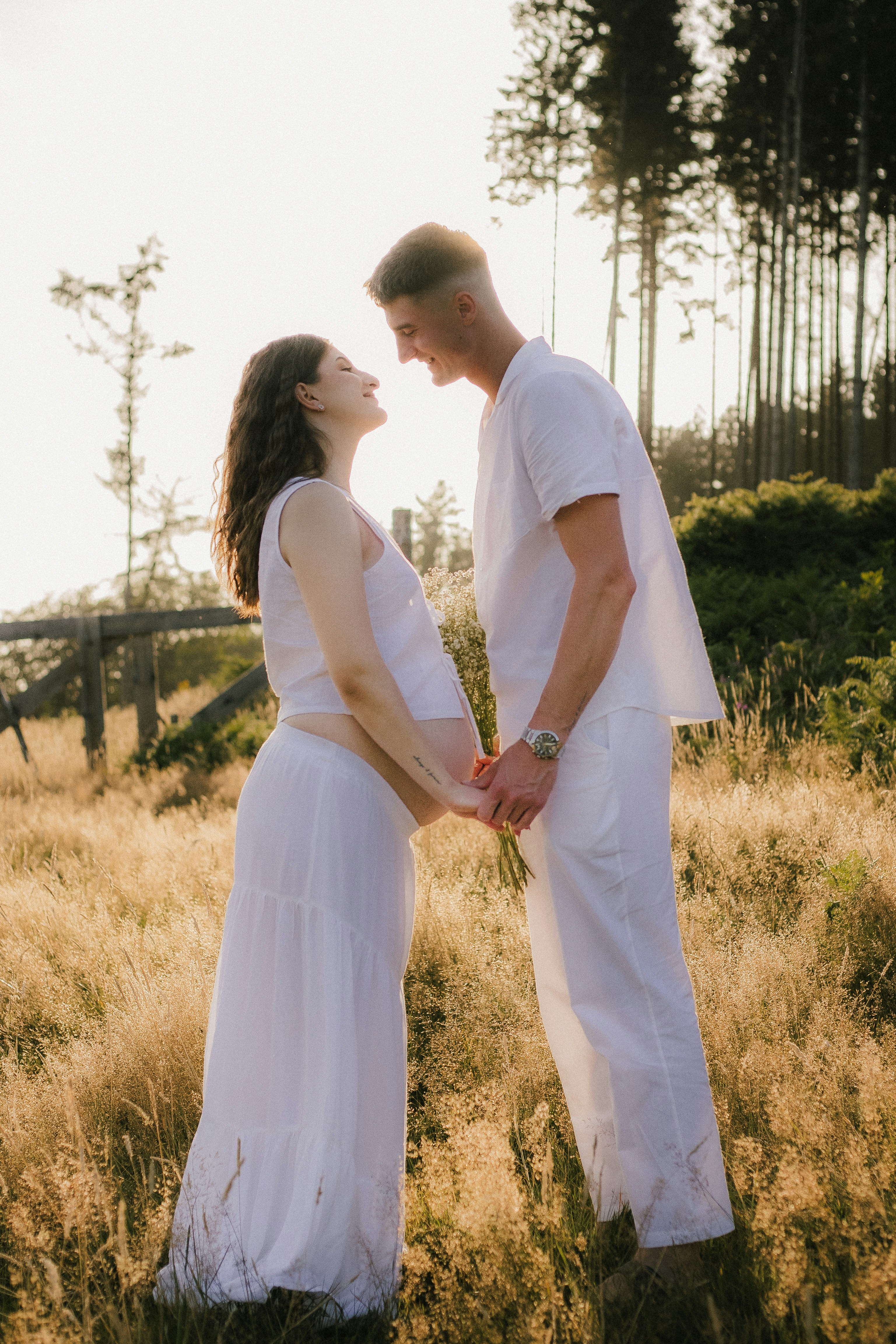 Expectant couple smiling and holding hands in a golden field.