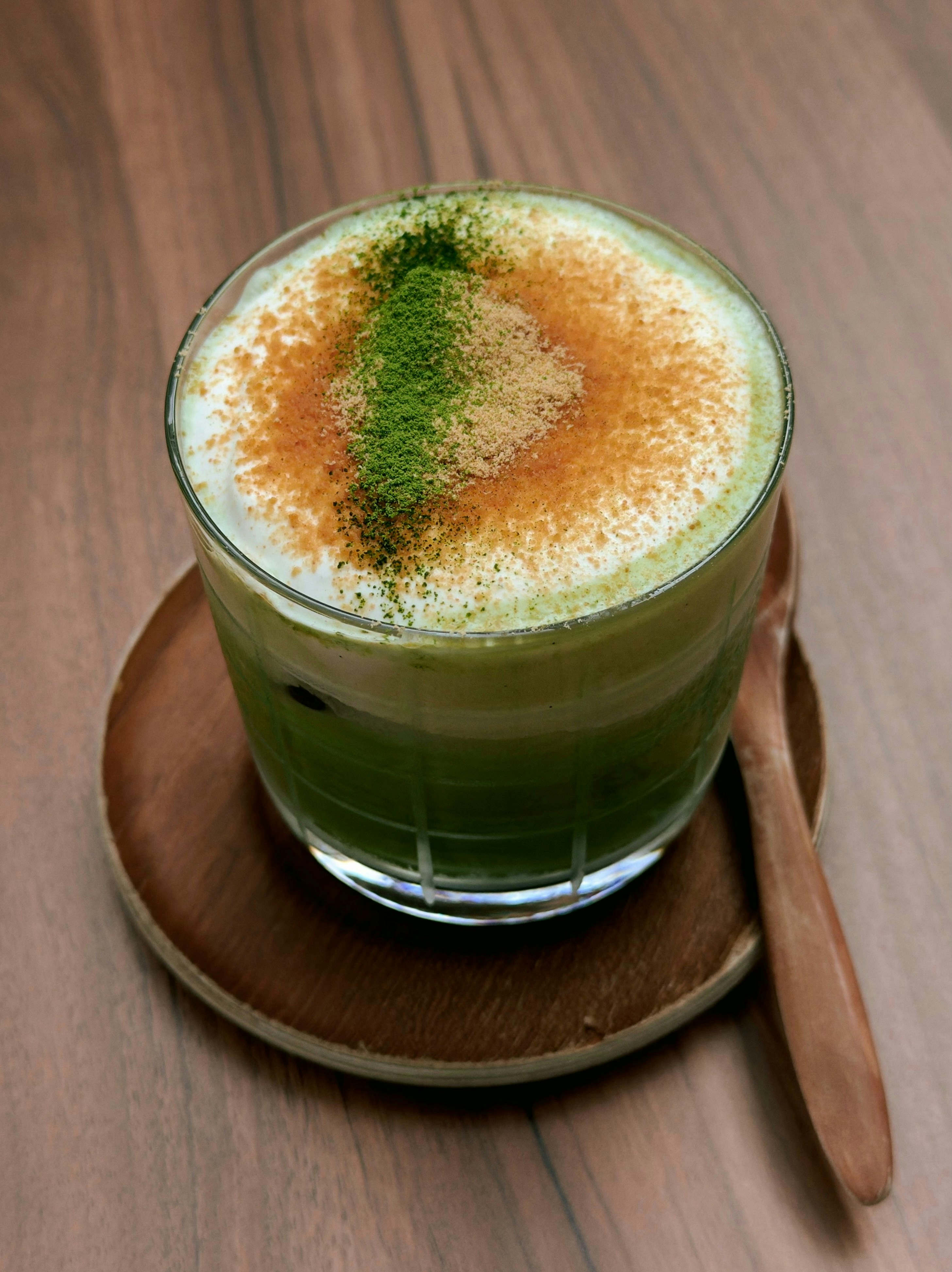 Iced matcha latte with powder on a wooden coaster