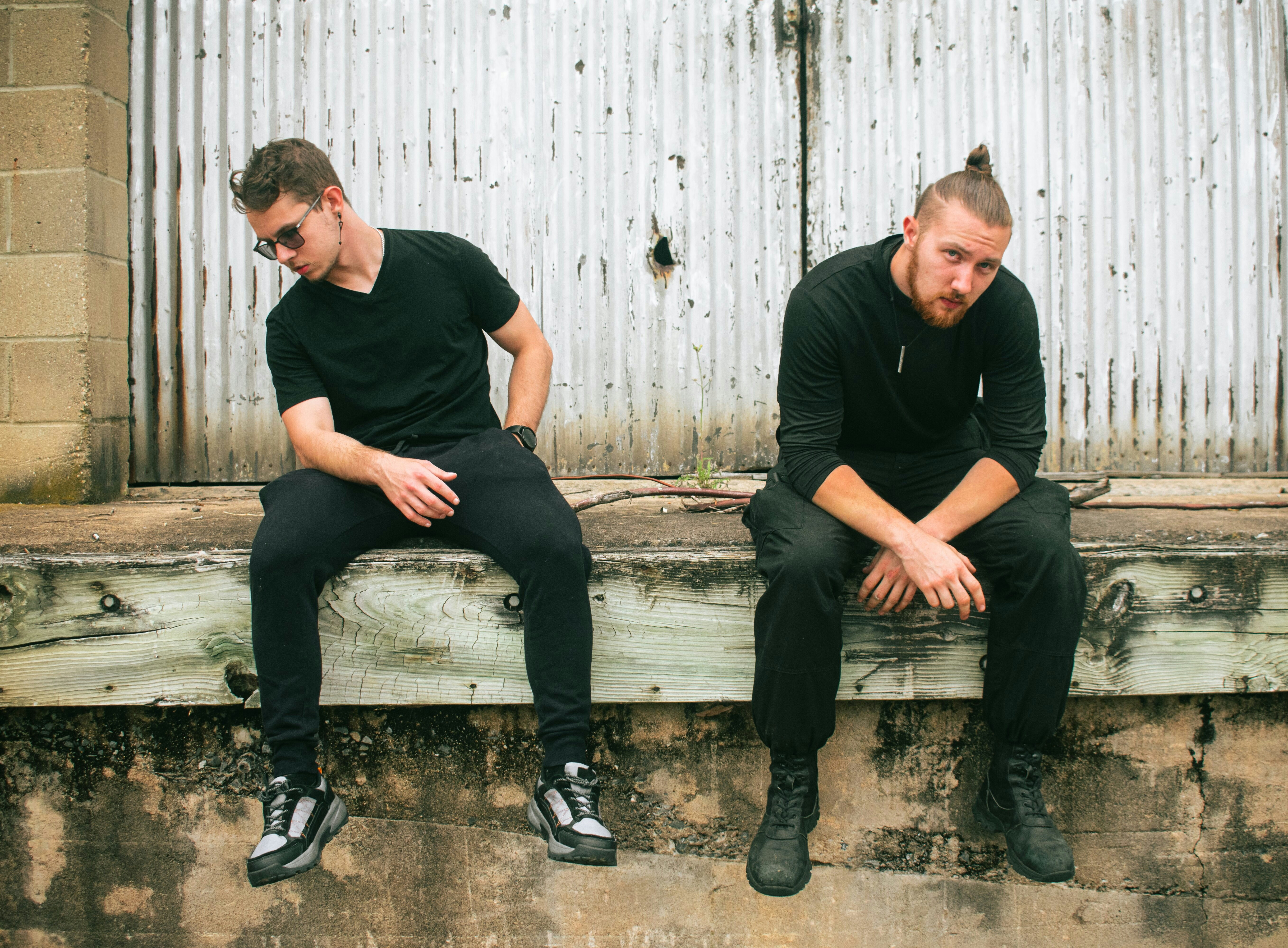 Two men in black clothes sitting on a wooden ledge