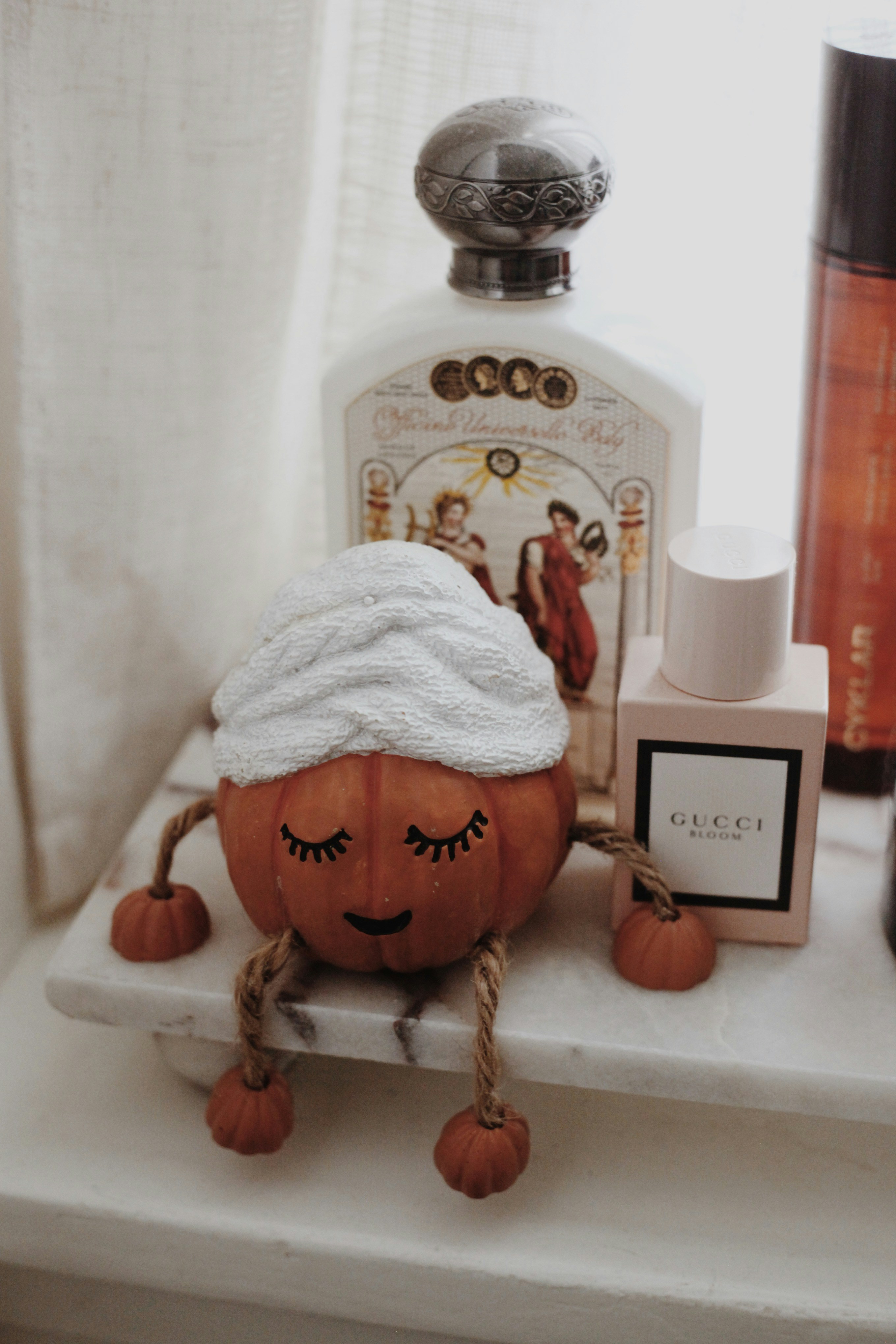 Plush pumpkin toy on a marble shelf with perfume bottles