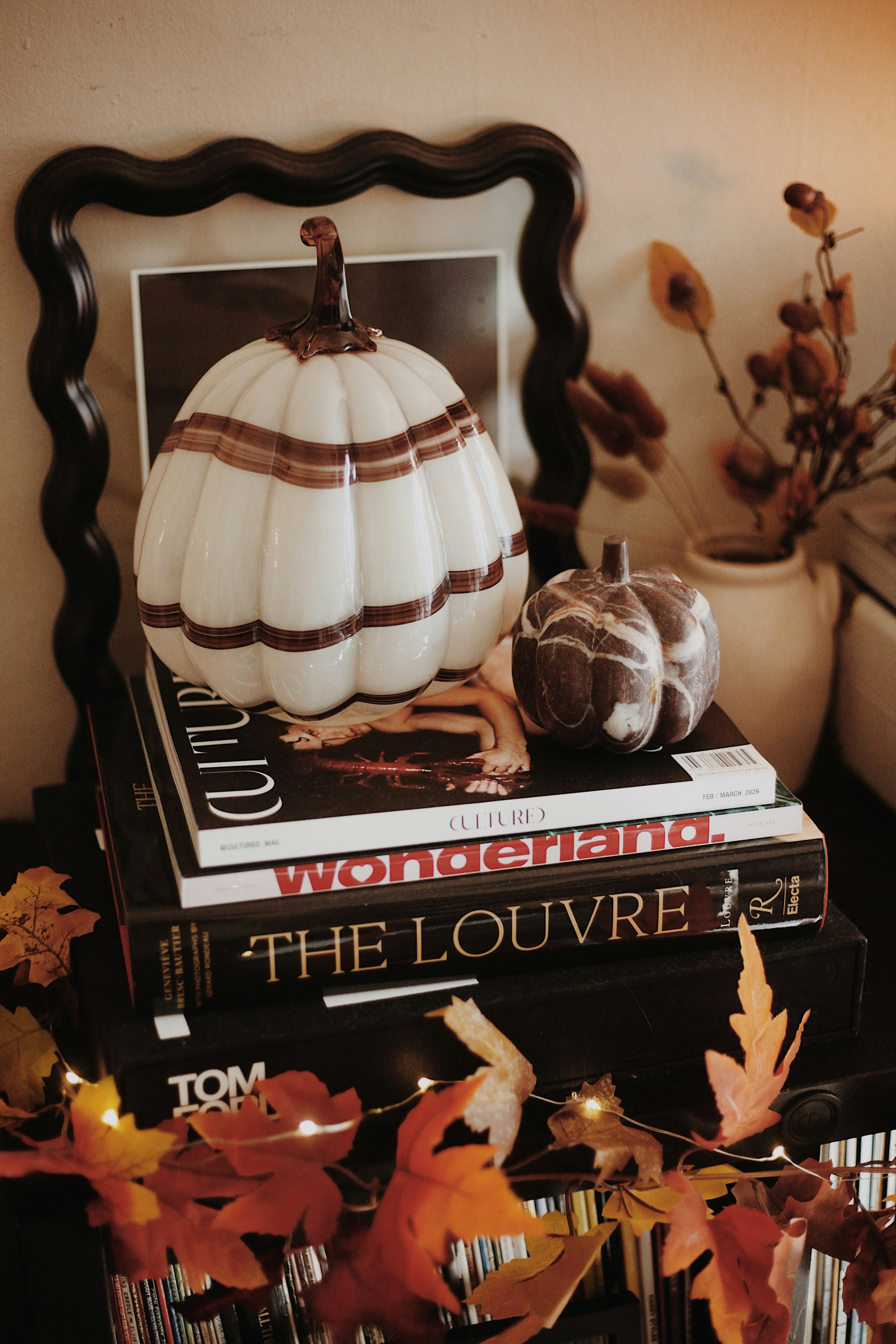 Autumn pumpkins, stacked art books, and a glowing leaf garland
