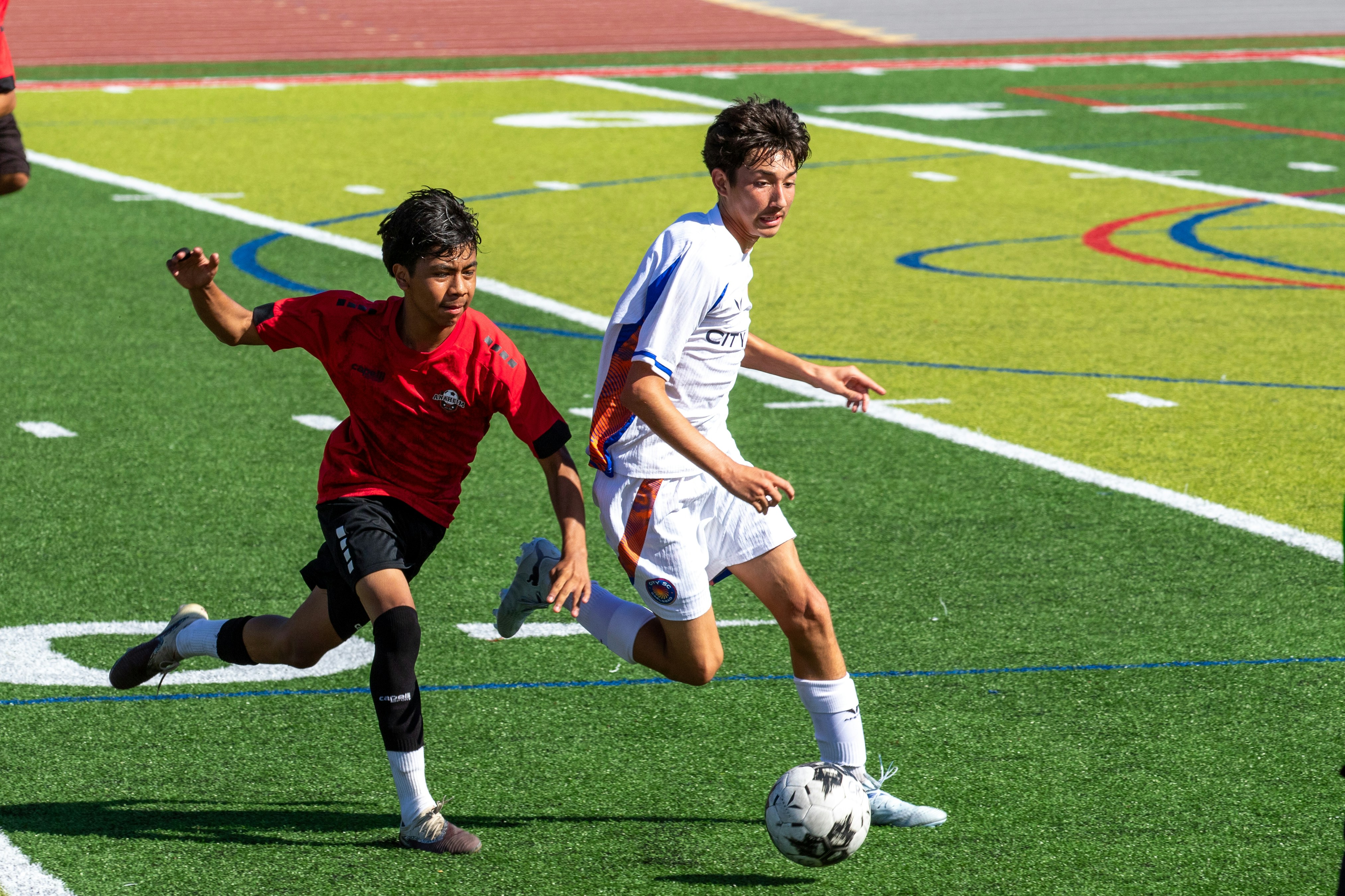 Two boys playing soccer on a sunny green sports field