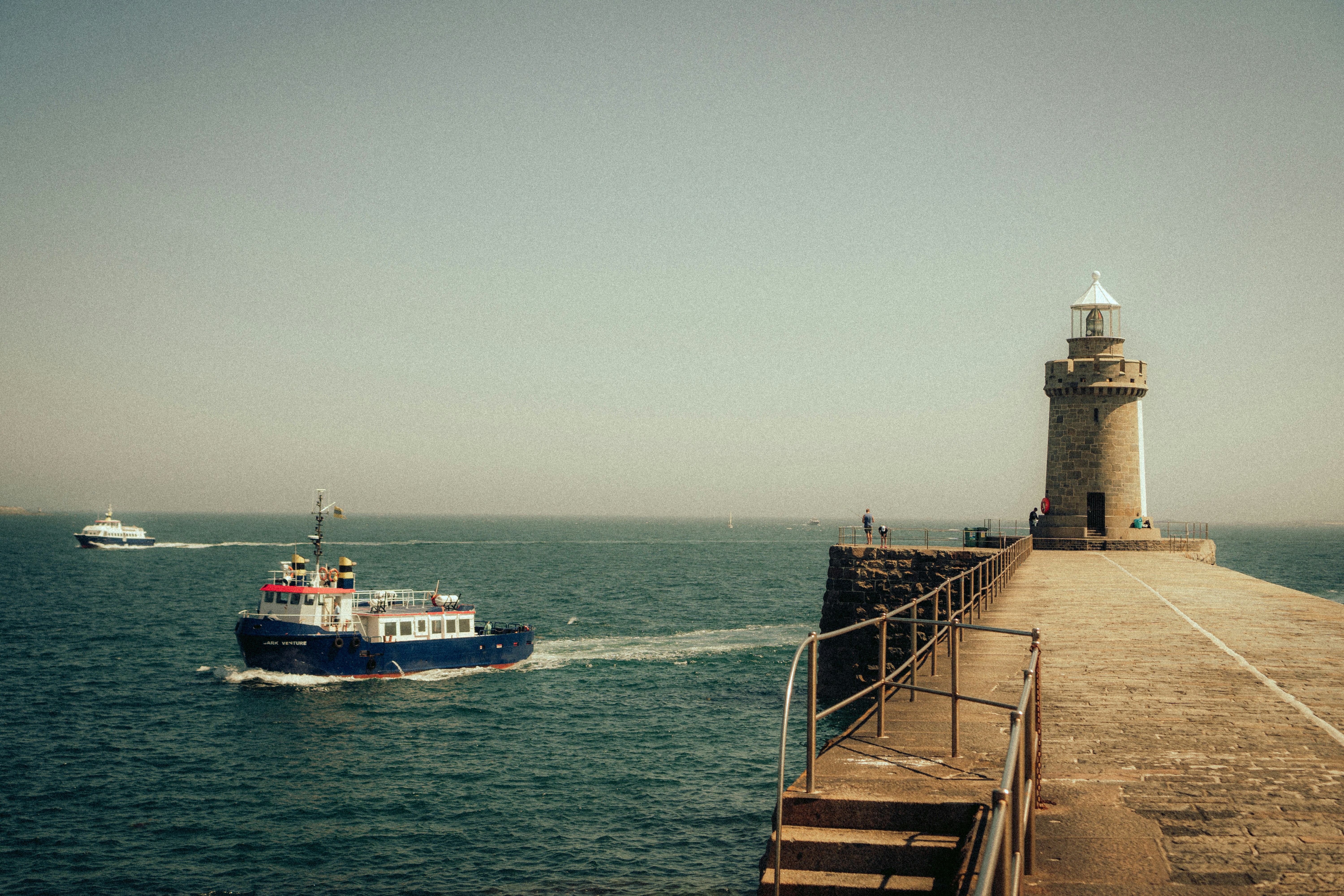 A boat sails past a lighthouse on a sunny day.