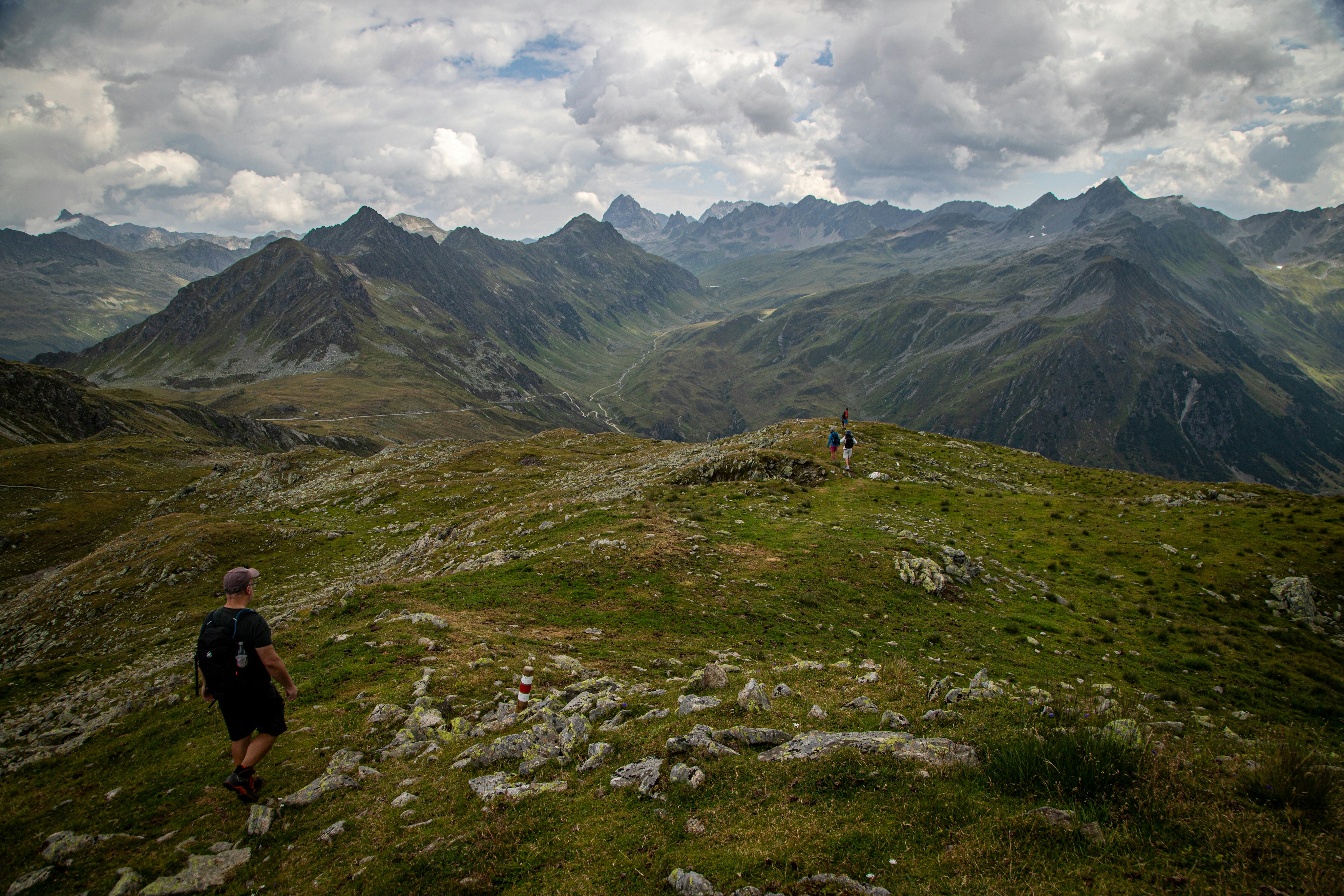 Hikers on a rocky mountain ridge under dramatic cloudy sky.