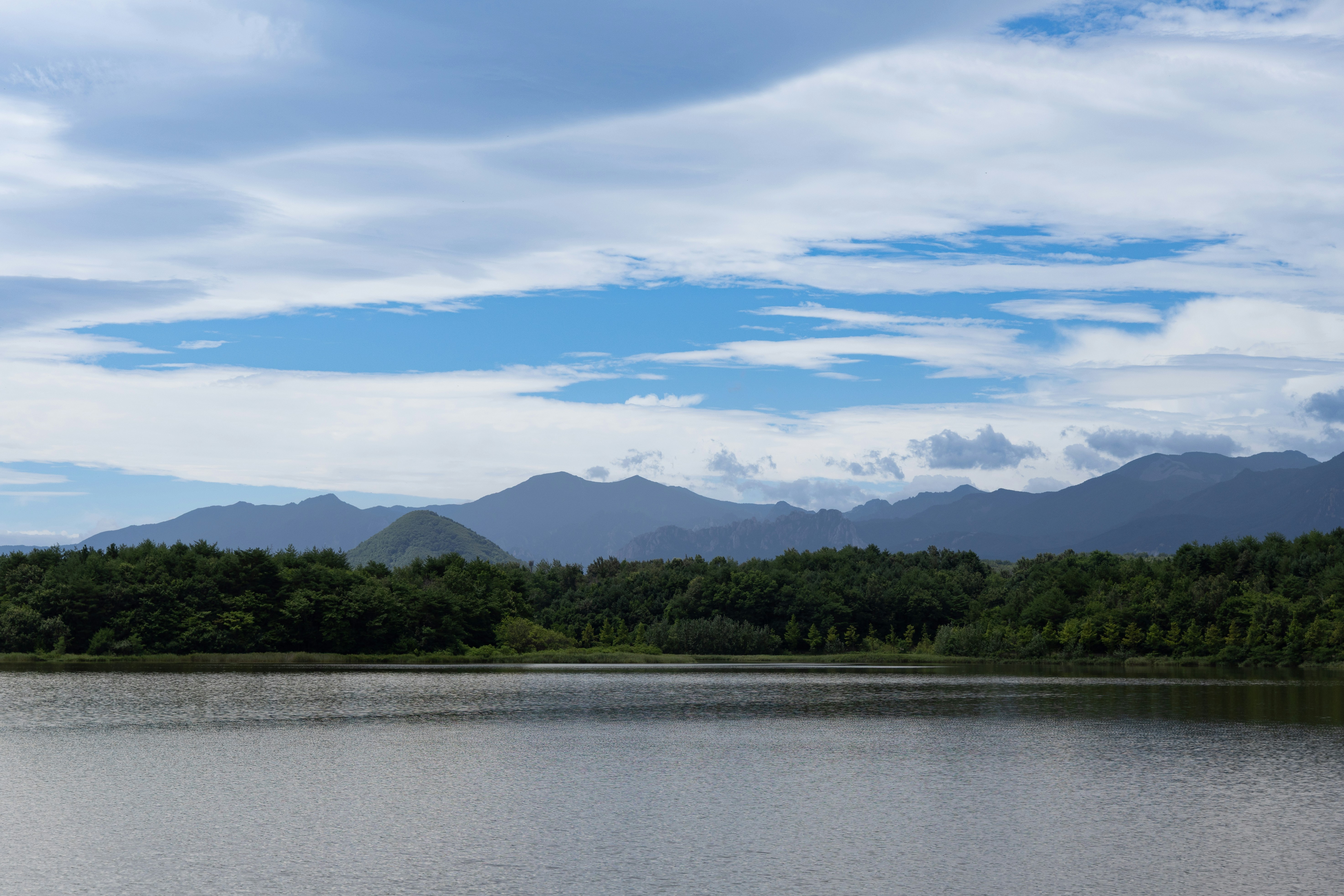 Calm lake, green trees, and mountains beneath a cloudy sky